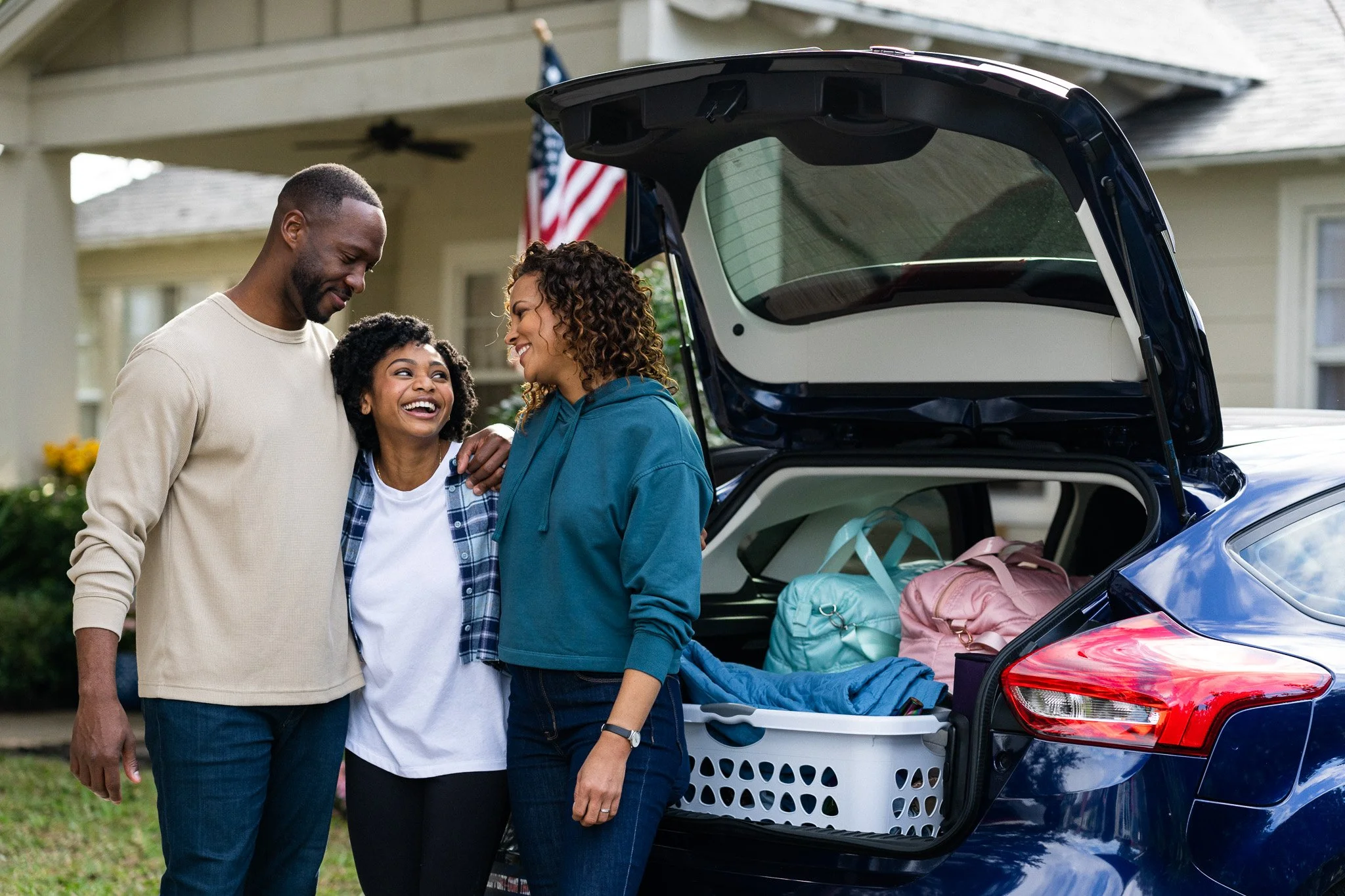 Family enjoying a moment together next to an open car trunk filled with bags and packing supplies