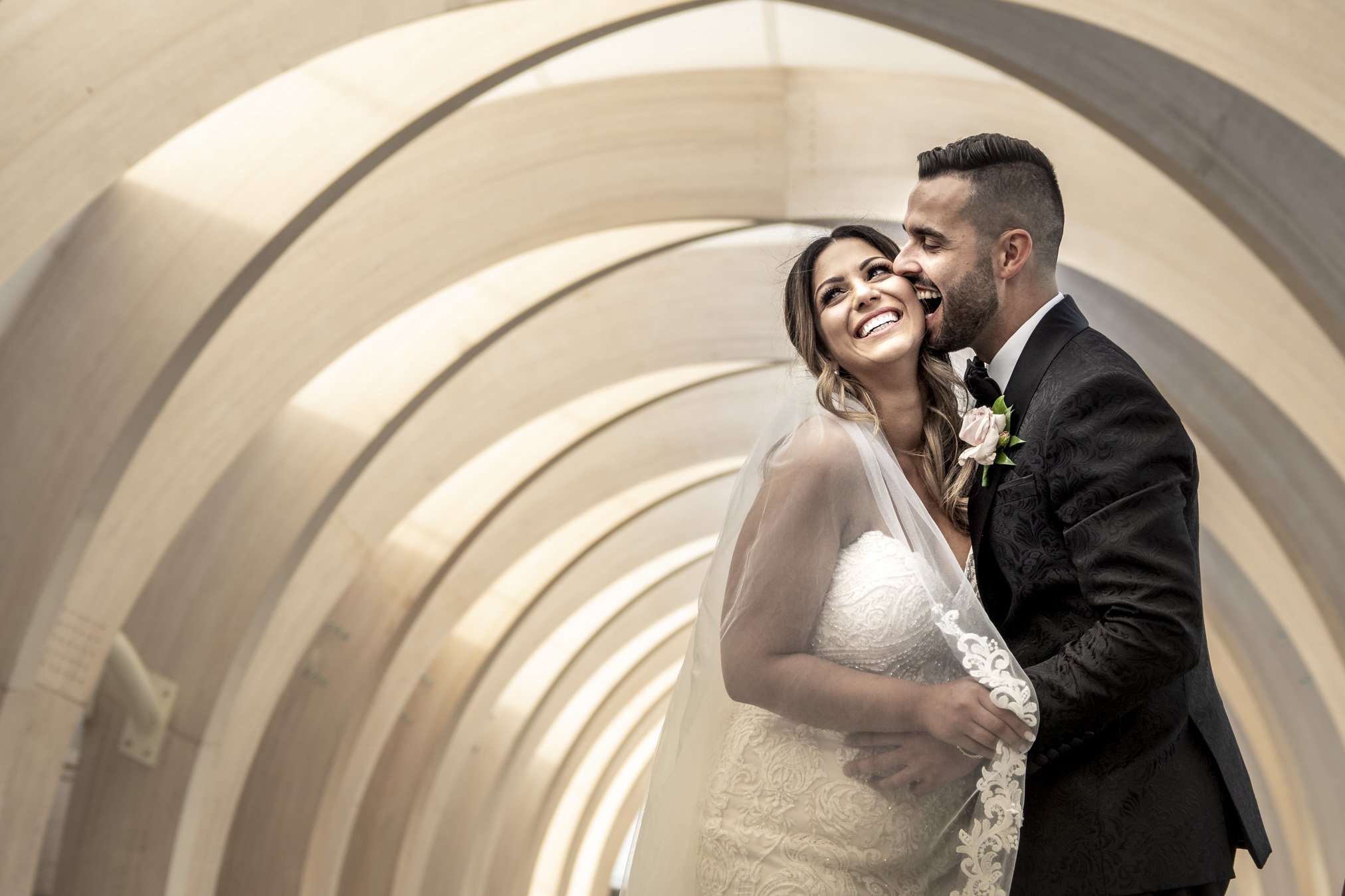 A happy bride and groom in wedding attire embracing inside a modern architectural tunnel.