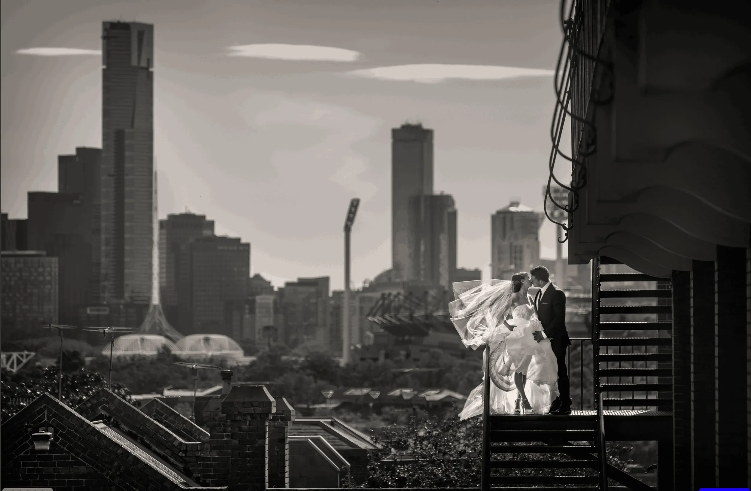 Black and white photo of a bride and groom on a fire escape balcony in an urban city skyline.