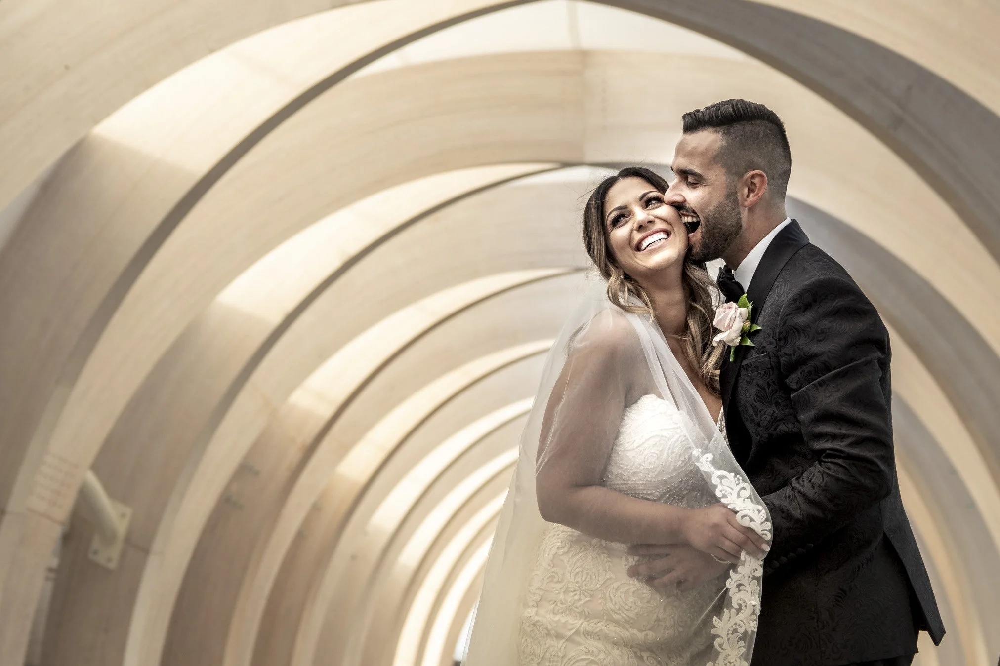 A happy bride and groom on their wedding day in a tunnel with a repeating curved arch pattern.