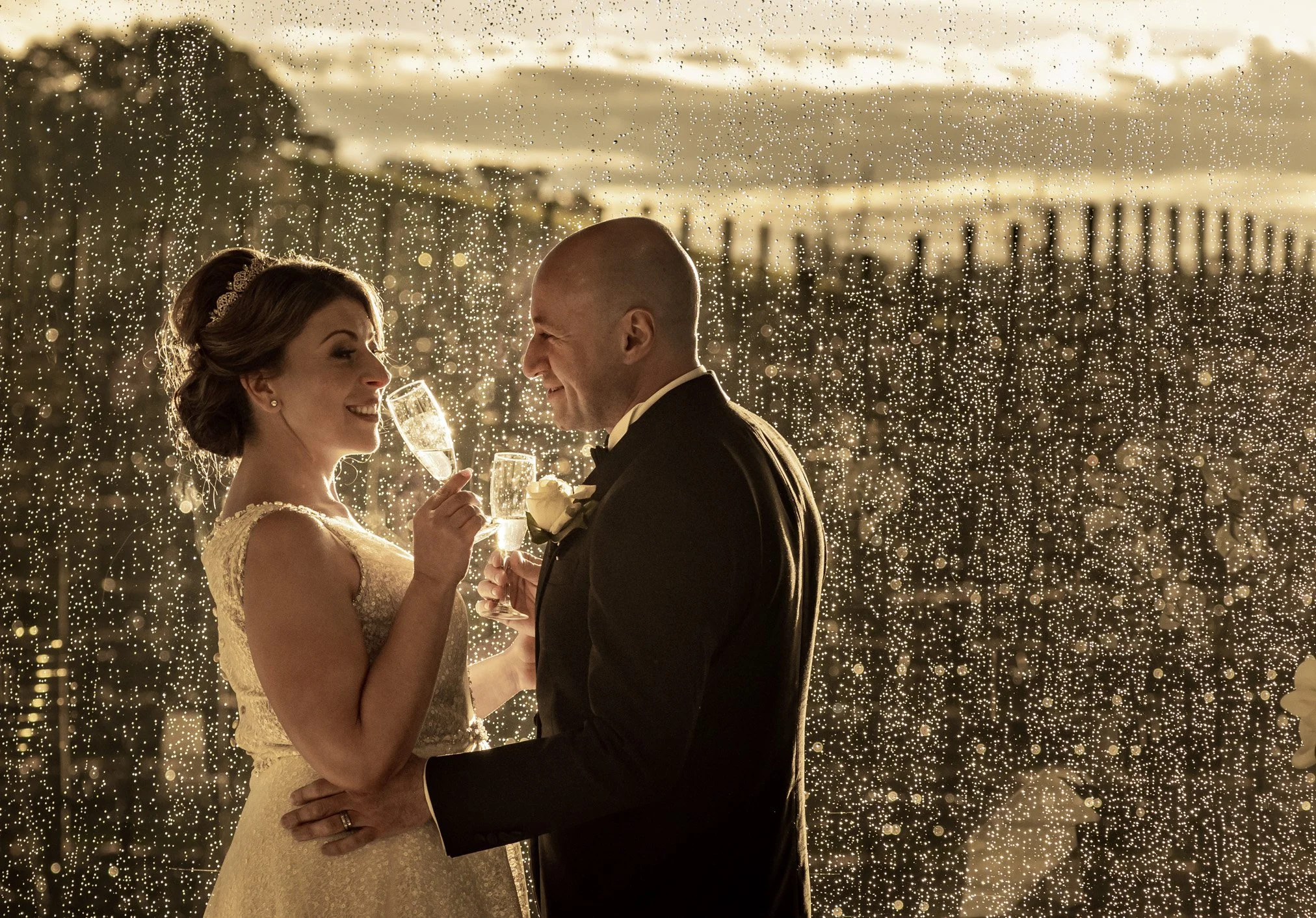 A bride and groom celebrating their wedding with champagne toasts in front of a rain of sparklers at sunset.
