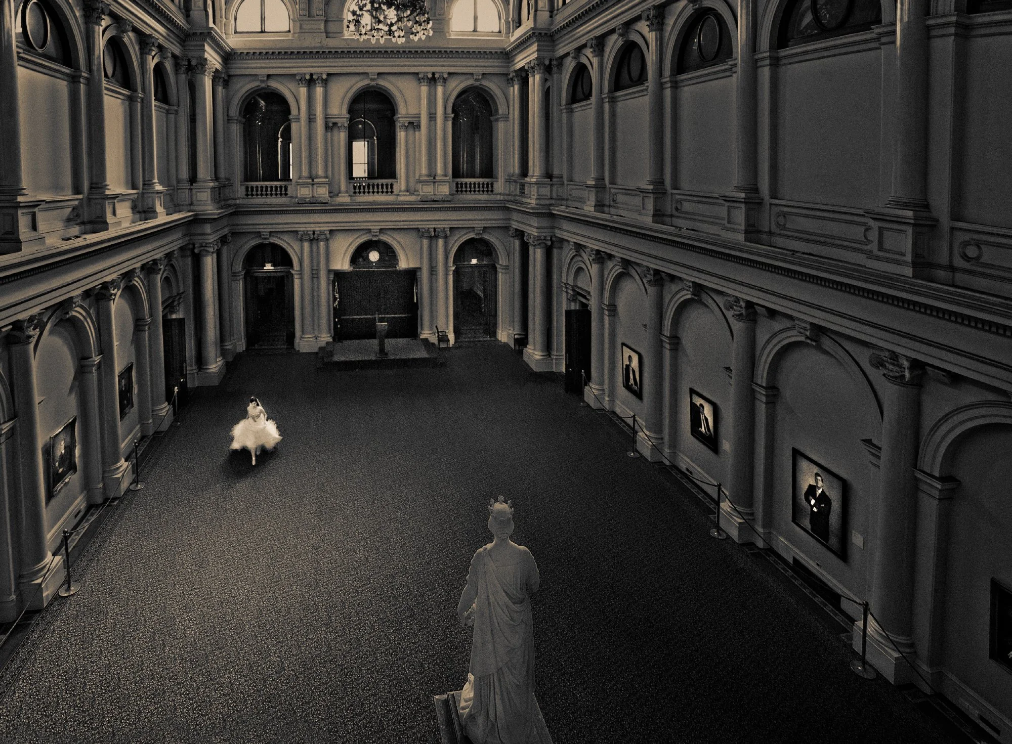 A woman in a white dress appears to be dancing in an art museum gallery with classical architecture, paintings on the walls, and a statue in the foreground.