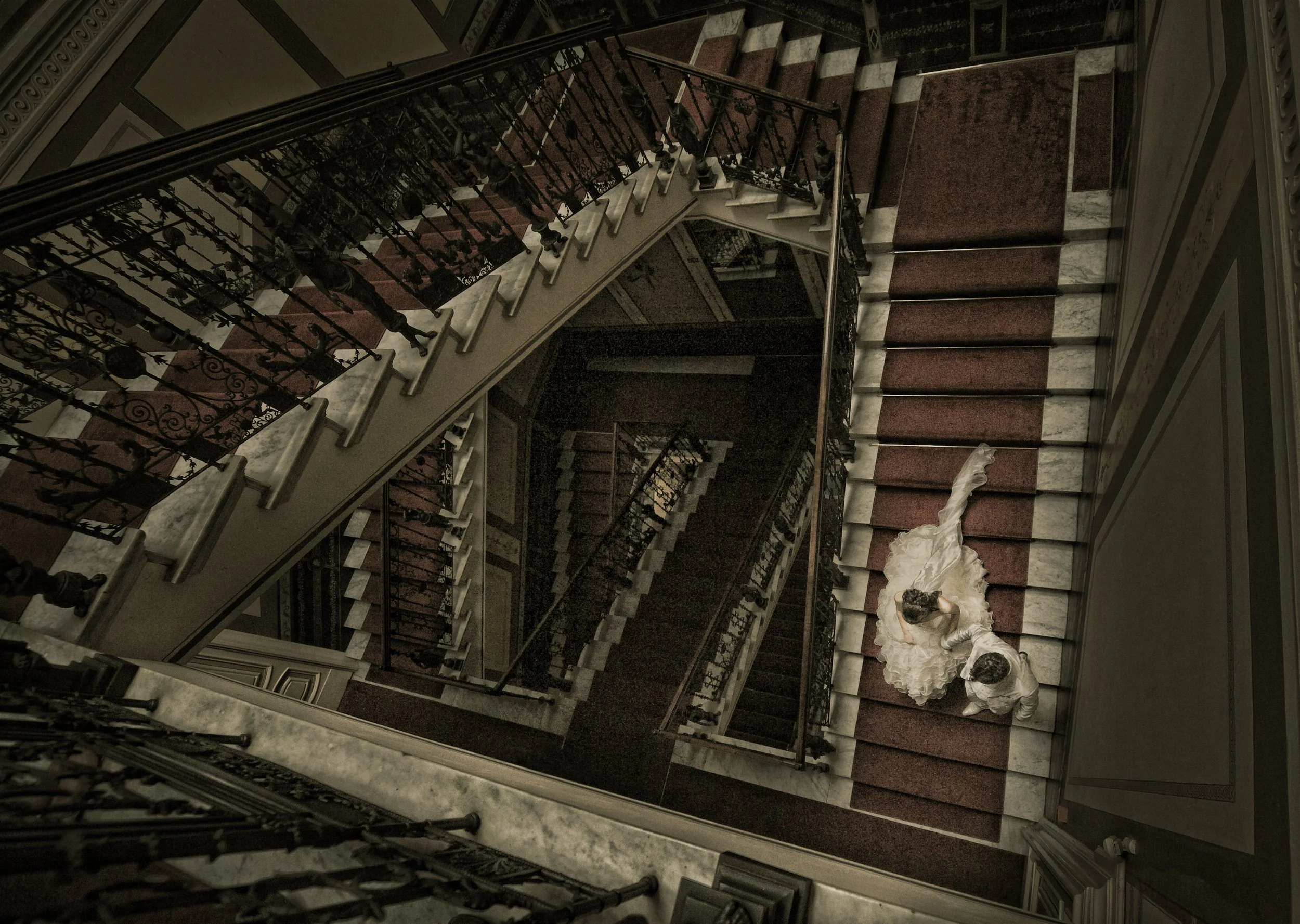 Wedding couple standing on a staircase with a red carpet in a grand, elegant interior