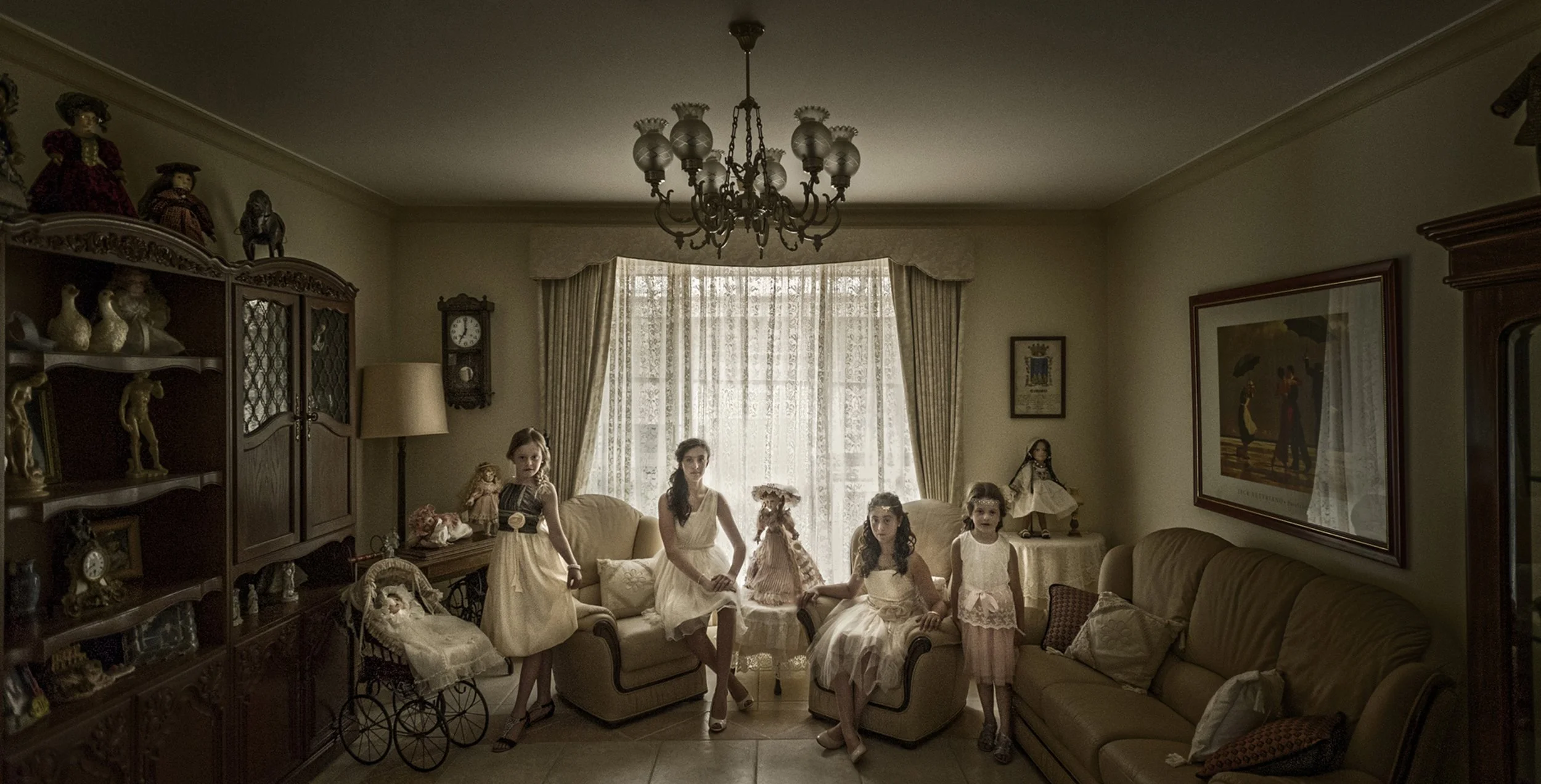 A vintage living room with five young girls in white dresses posing, surrounded by antique furniture, dolls, and a chandelier, with sunlight streaming through lace curtained windows.