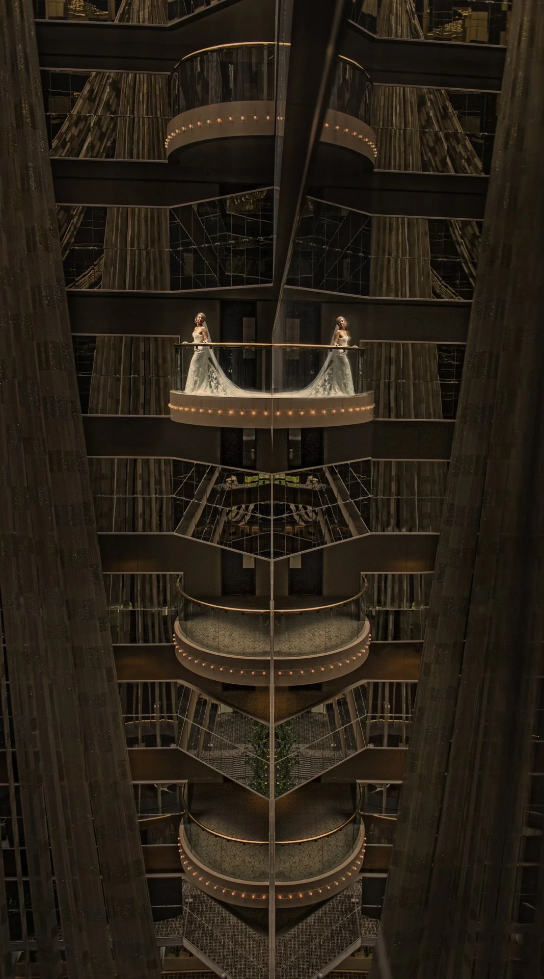 Multiple balconies inside a modern, mirrored building with warm lighting, reflecting a woman in a wedding dress on the top balcony.