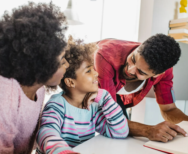 Three people, two adults and a child, smiling and engaging in a conversation or activity at a table in a bright room.