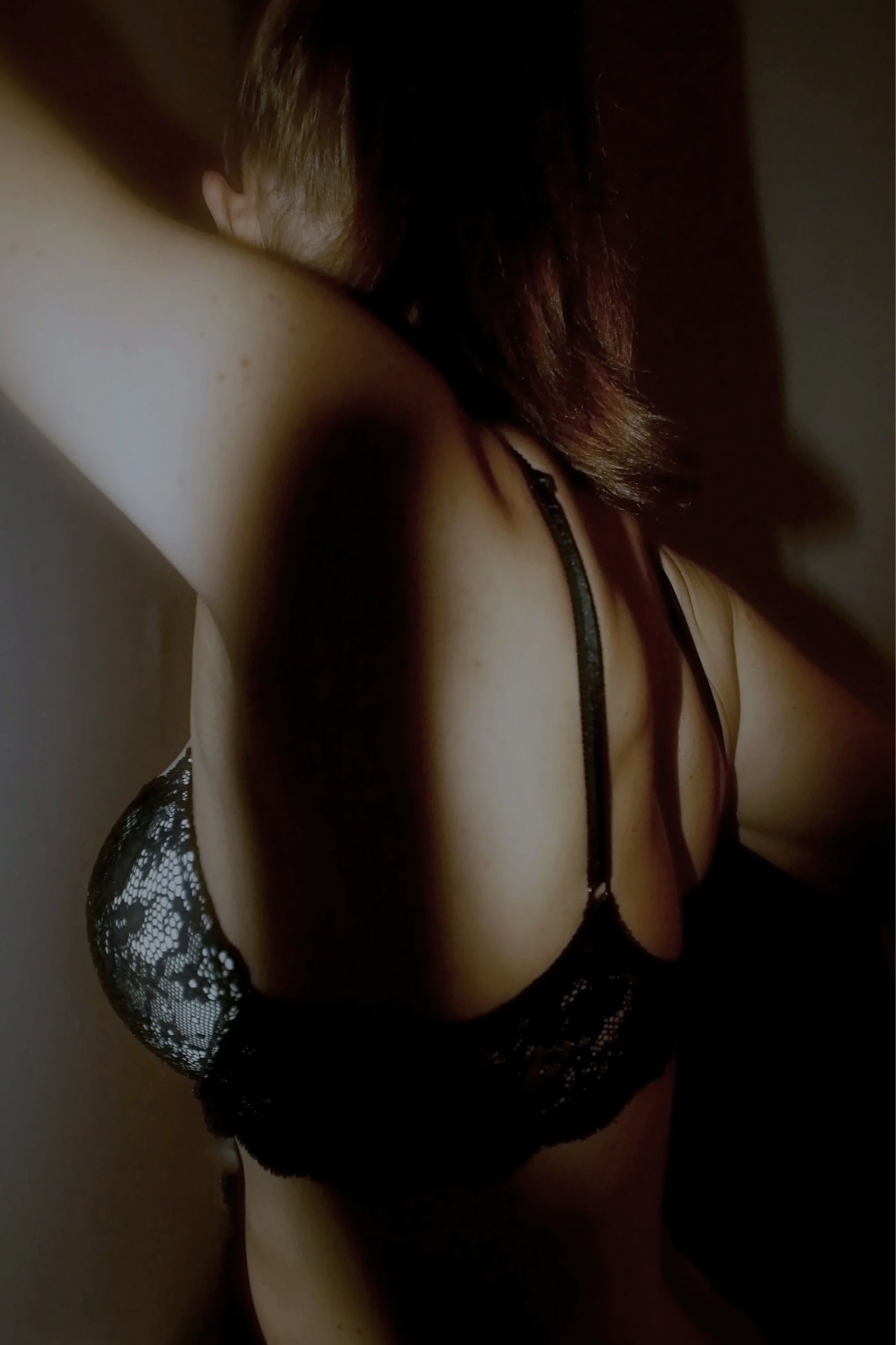 Close-up of a person wearing black lace lingerie, with a focus on the shoulder, arm, and hair.