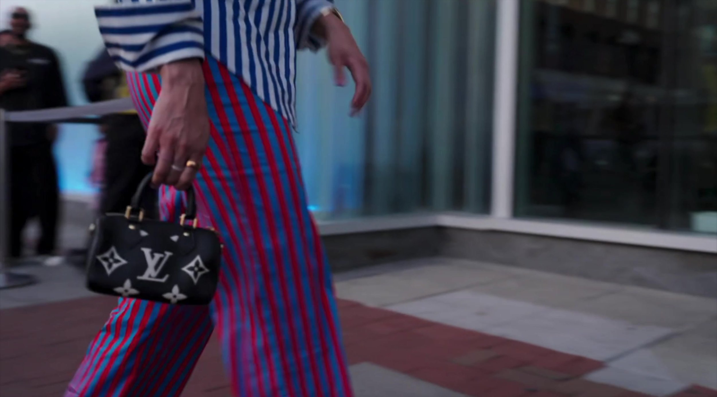 Robyn Dixon in red-and-blue striped trousers carrying a small black Speedy-style bag with an oversized beige embossed LV monogram.