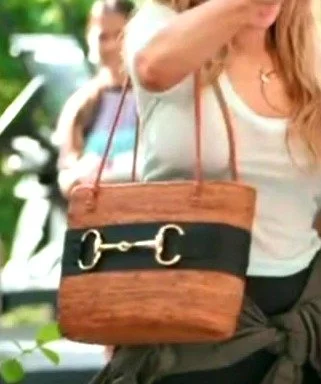 Close-up of Daisy Toye's rattan basket tote with tan leather handles, a black leather band and a gold horsebit-style bit.