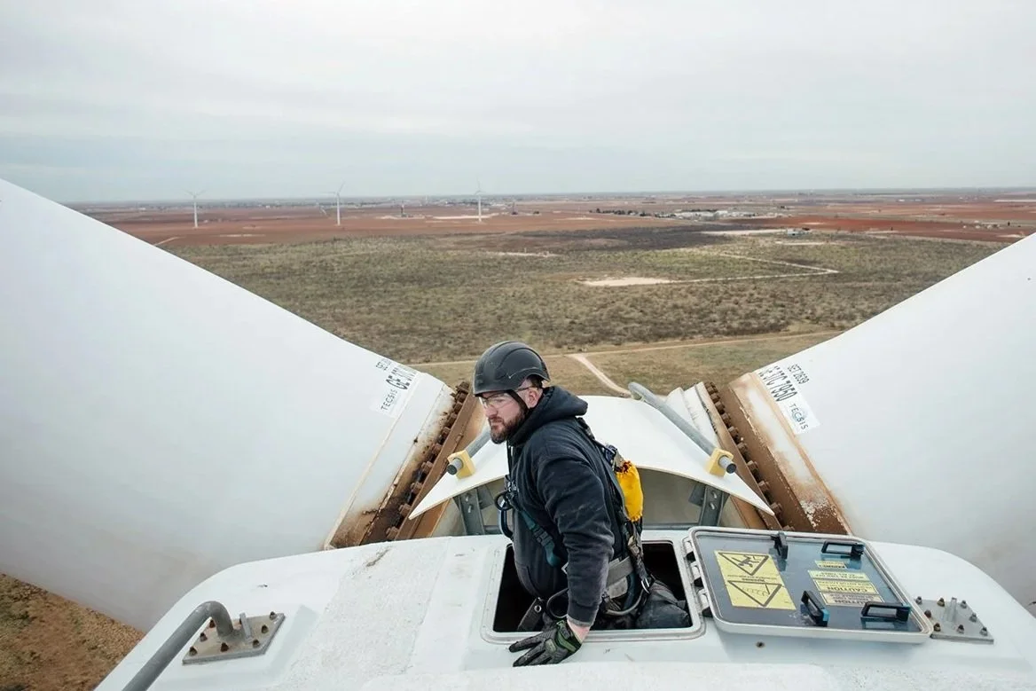 View the Energy in Transition dossier: a wind technician works atop a turbine above an open landscape.