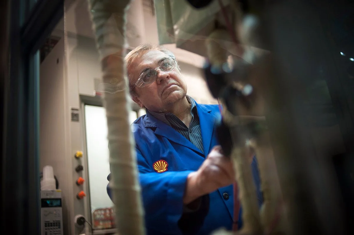 A Shell technician in blue coveralls inspects industrial equipment inside a processing facility.