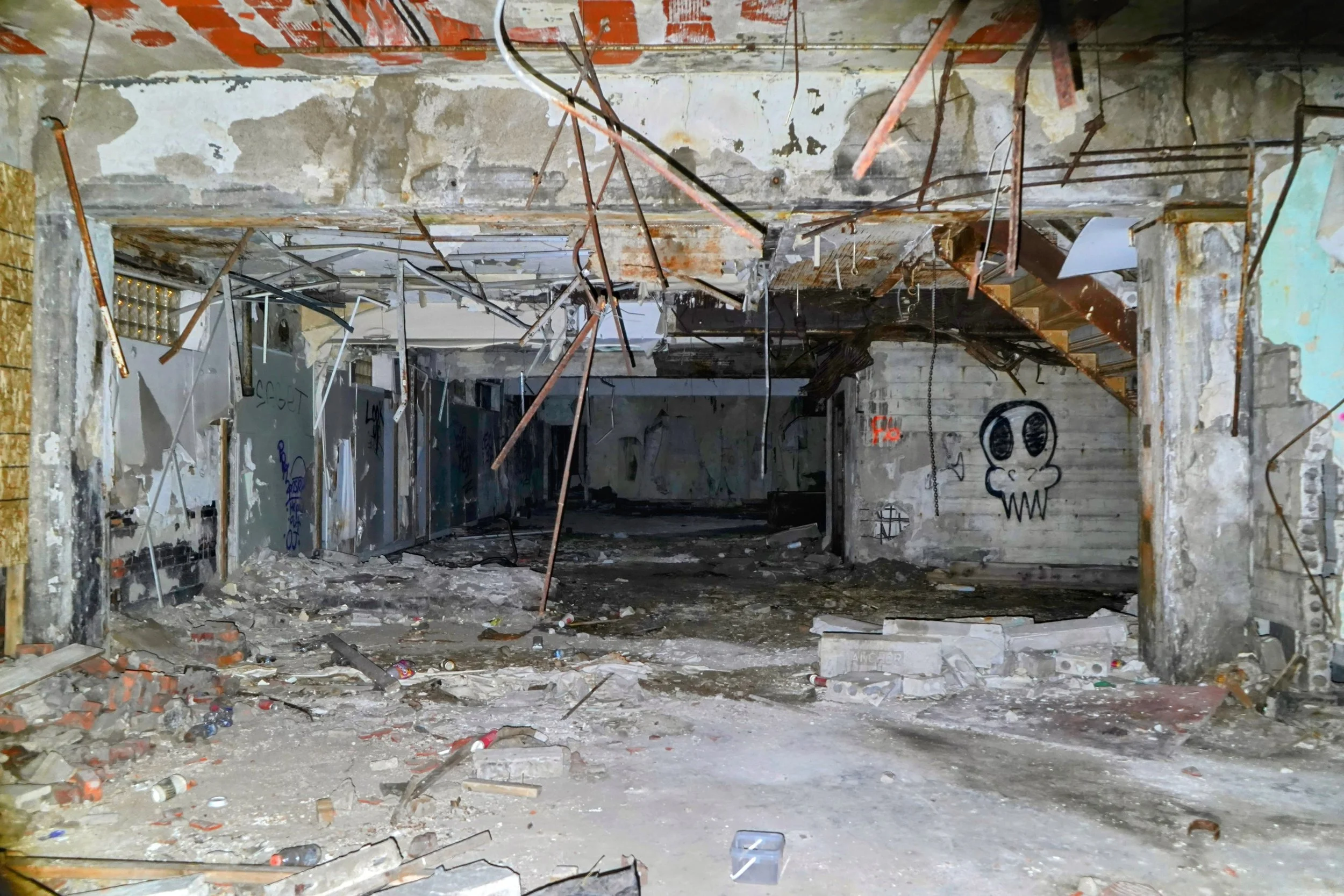 Abandoned building interior with graffiti on walls, debris, and exposed ceiling wires.