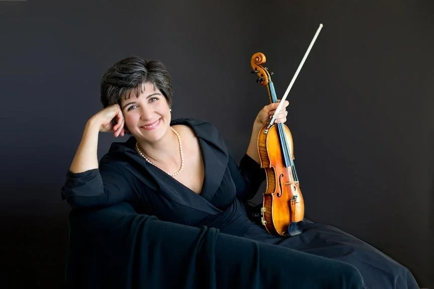 A violinist wears all black while reclining on a black couch.