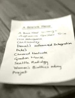 A handwritten list on a piece of paper sitting on a desk with items like Denali Advanced Integration and Duke's Chowderhouse