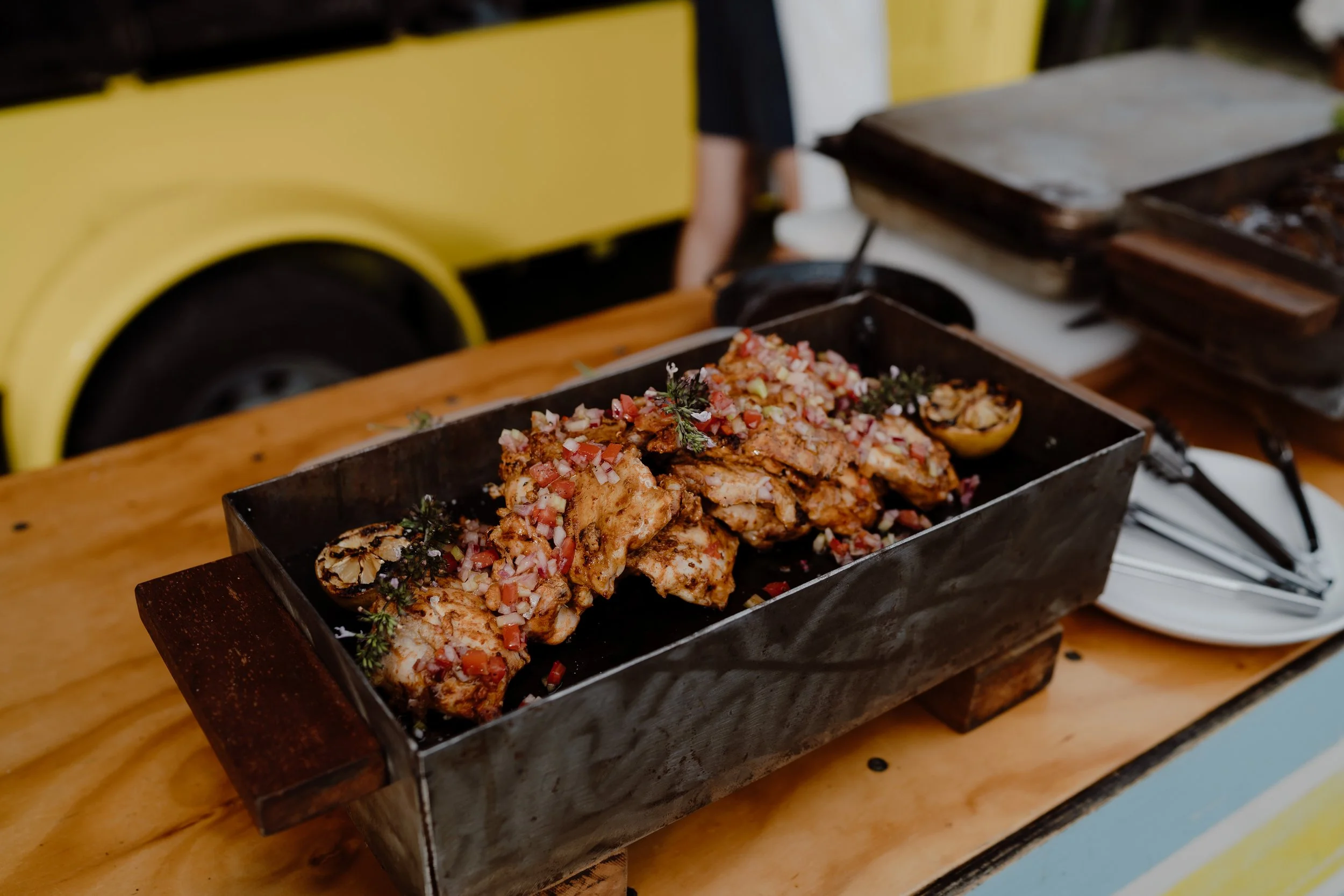 Grilled chicken topped with chopped onions, tomatoes, and herbs on a metal tray