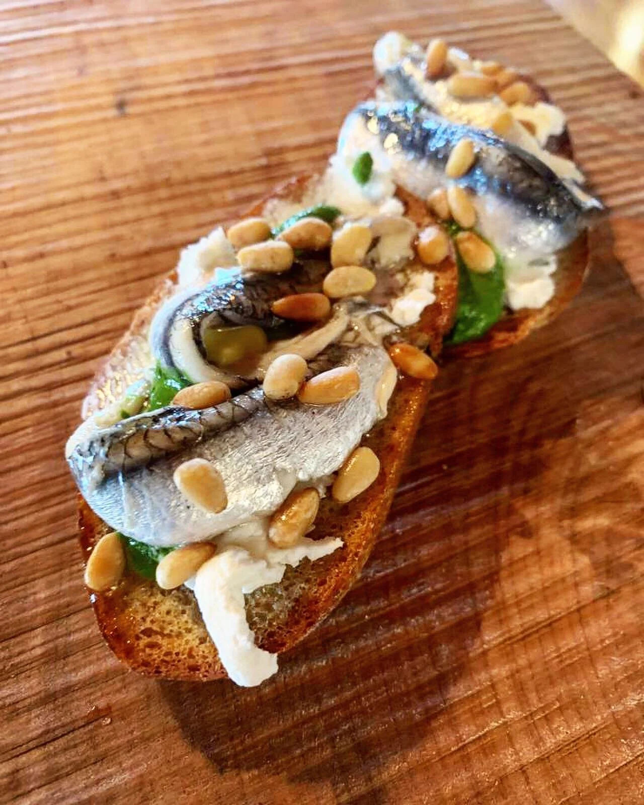 Open-faced sandwich with sardines, pine nuts, green peppers, and cheese on toasted bread, served at an event, possibly a wedding.