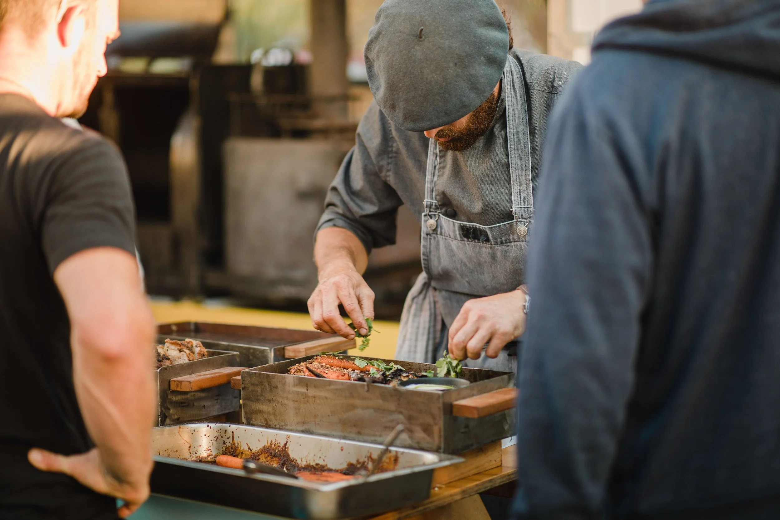 Chef garnishing grilled meats on a barbecue grill for guests at a catered event.