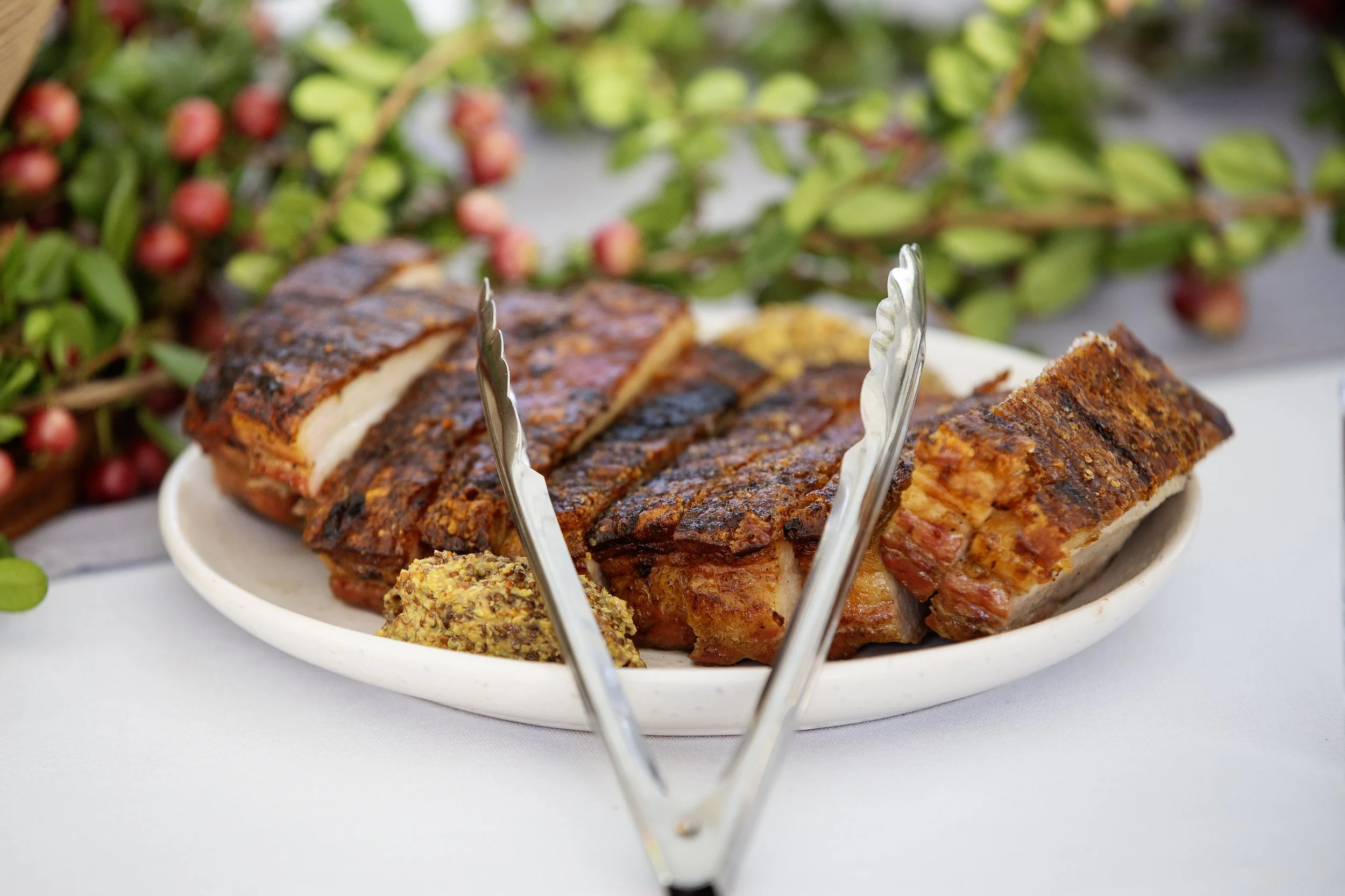 Platter of smoked ribs with sauce on the side and a sprig of greenery in the background, catered event.