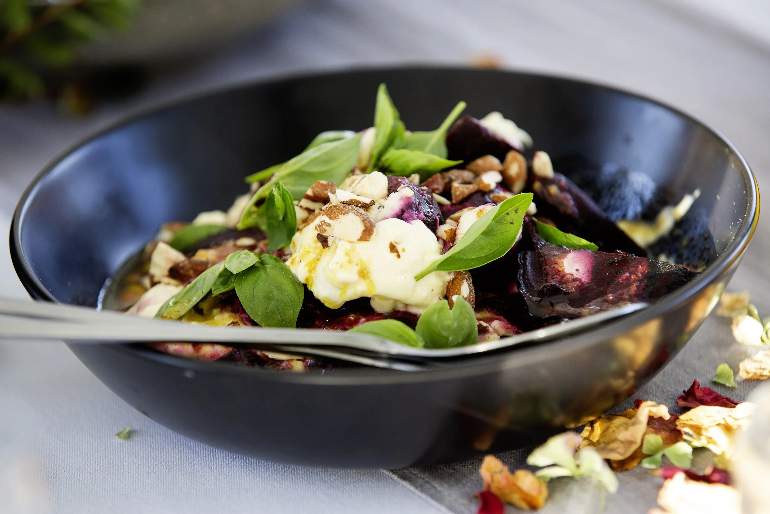 Berry salad with basil leaves and nuts in a black bowl.