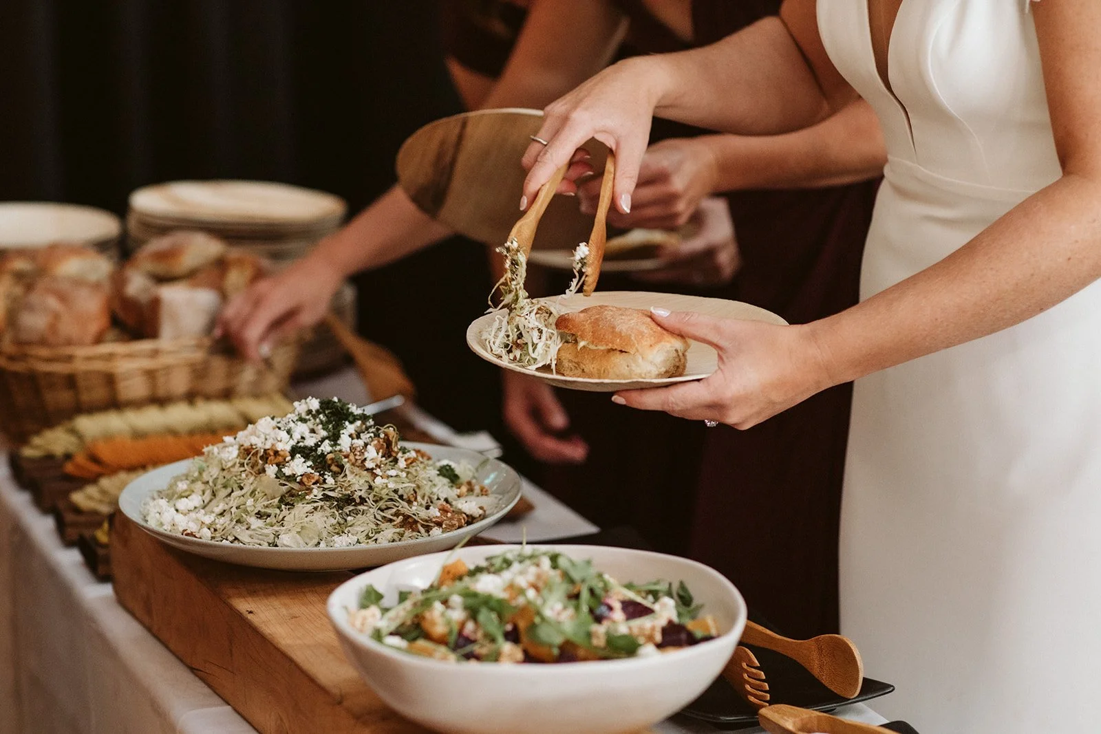 People serving themselves food at a buffet, where the event has been catered, with salads and bread on the table.