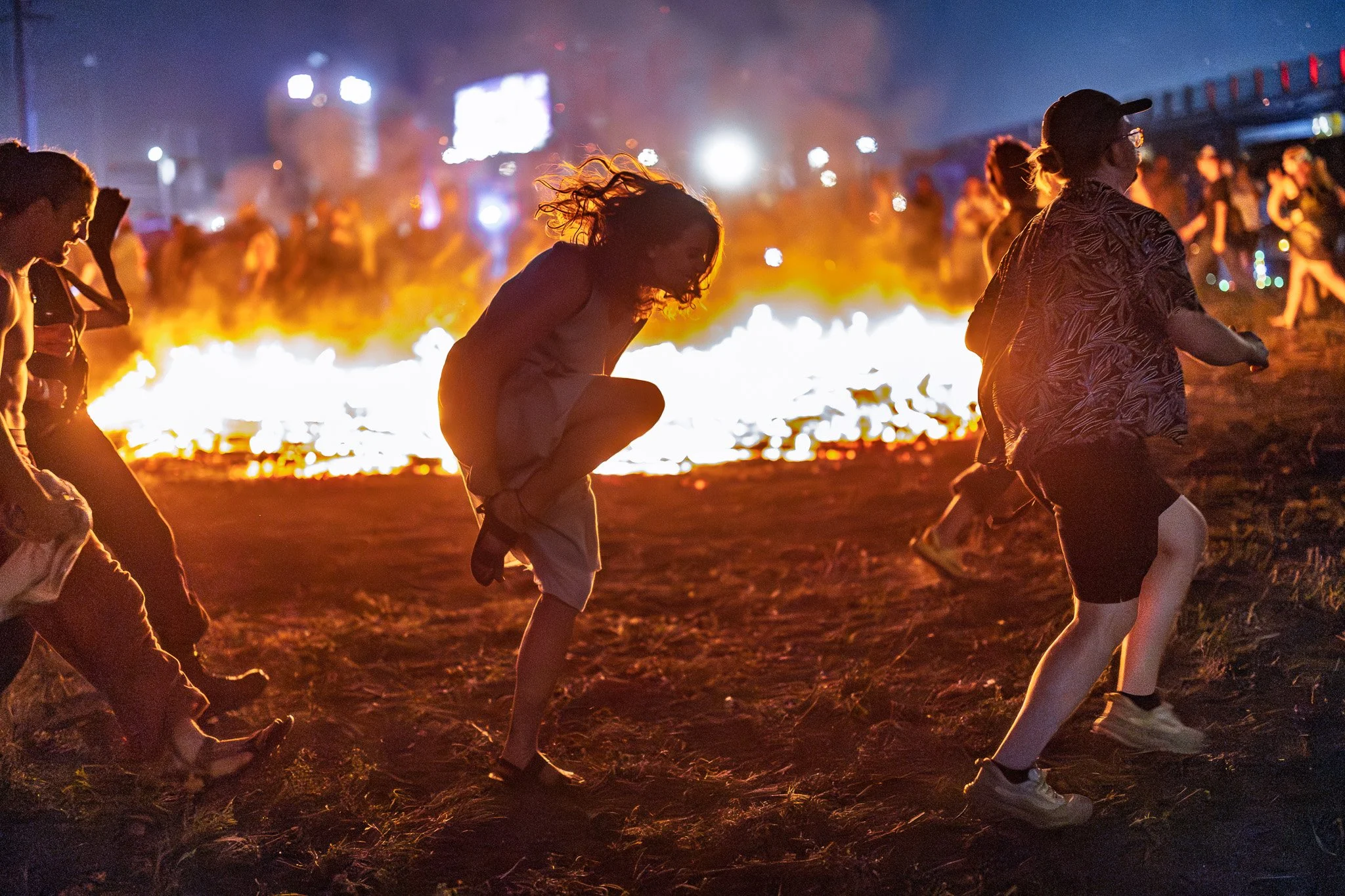 People running near a large campfire at night during a festival or outdoor event.