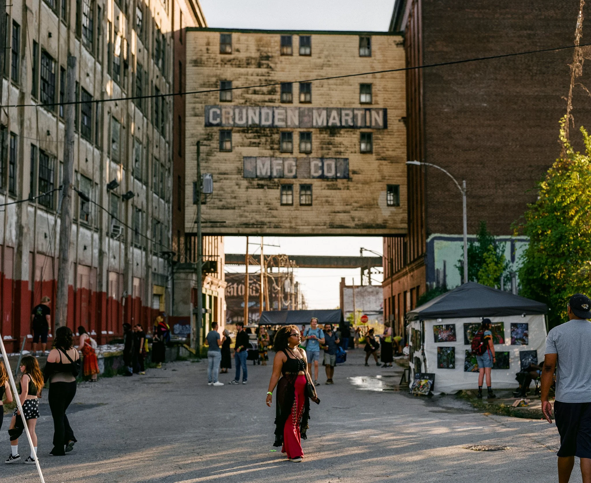 An outdoor scene at an event with people walking and standing, tents, and a building with a sign reading 'Chunden Martin MFG Co.' in the background.