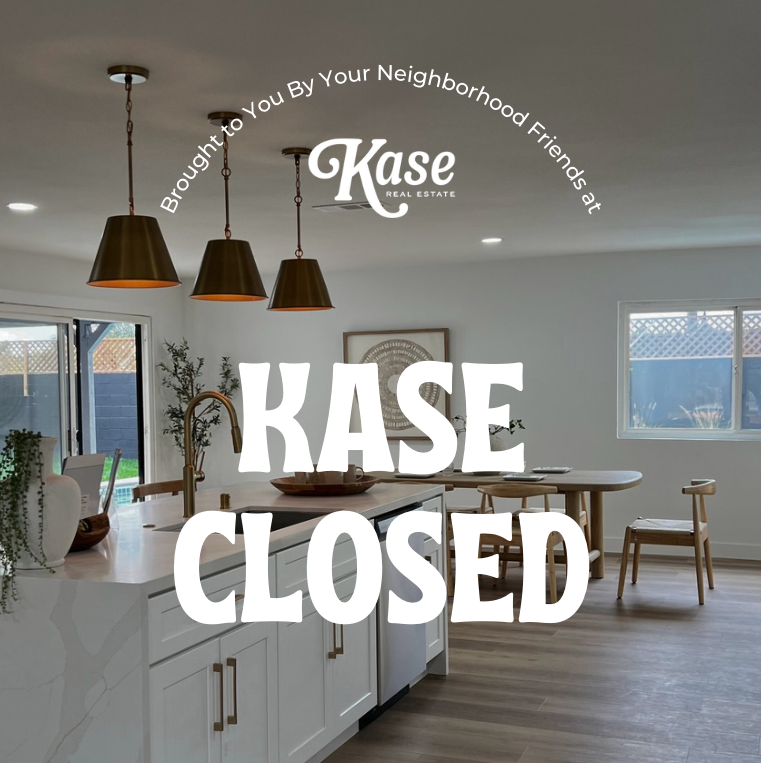A modern kitchen with white cabinets, wooden dining table, and pendant lights. The image has text indicating the house is closed by Kase Real Estate.
