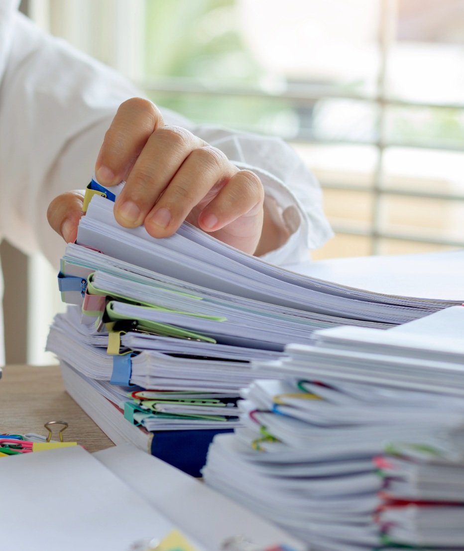 A person flipping through a large stack of organized papers and files on a desk.