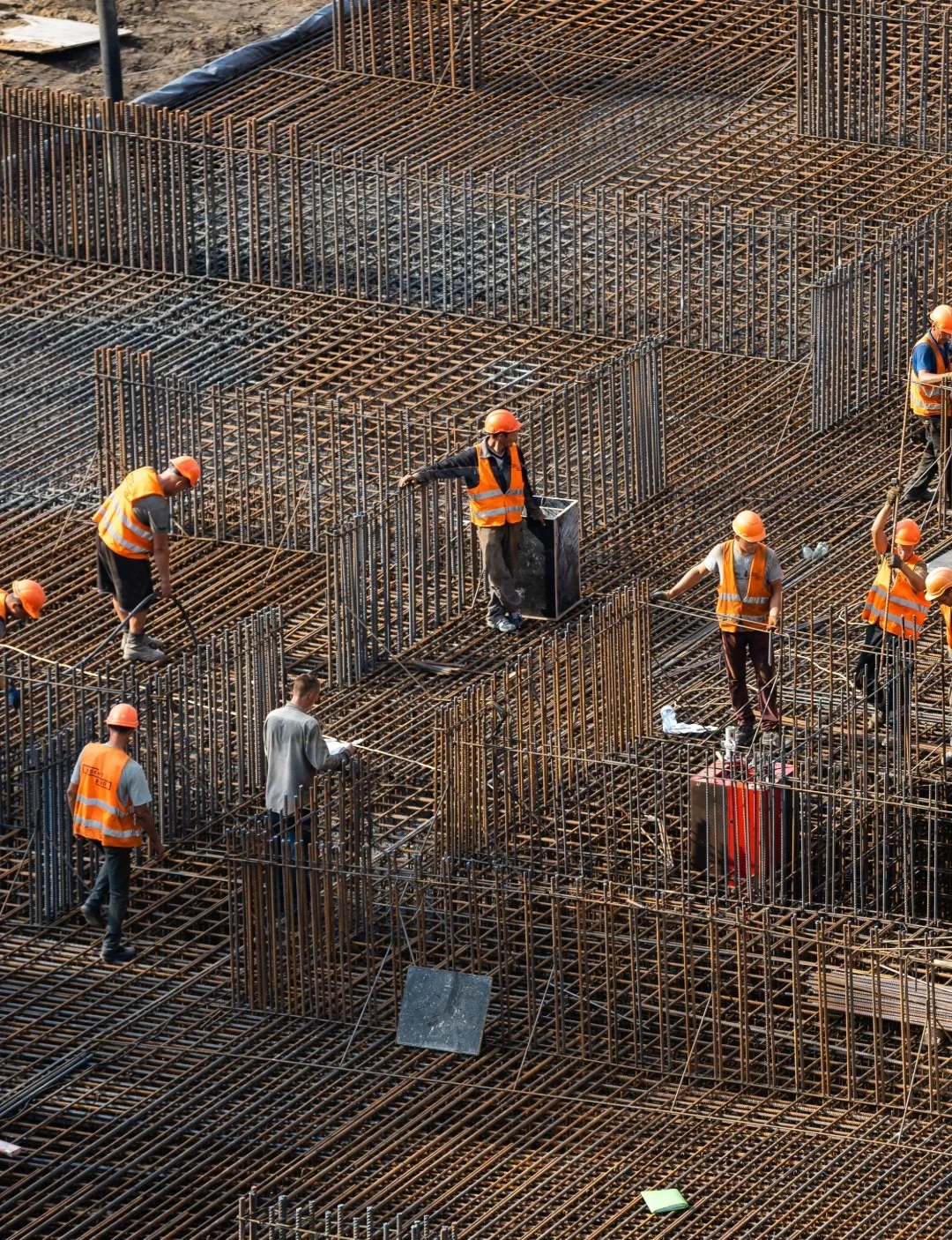Construction workers in orange safety vests and helmets working on steel rebar framework for a building under construction.