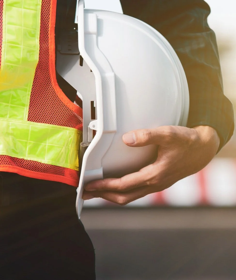 Person wearing a safety vest holding a white helmet.