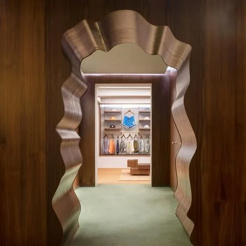 A wavy, irregularly shaped wooden doorway leading into a walk-in closet with shelves, hanging clothes, and storage boxes.