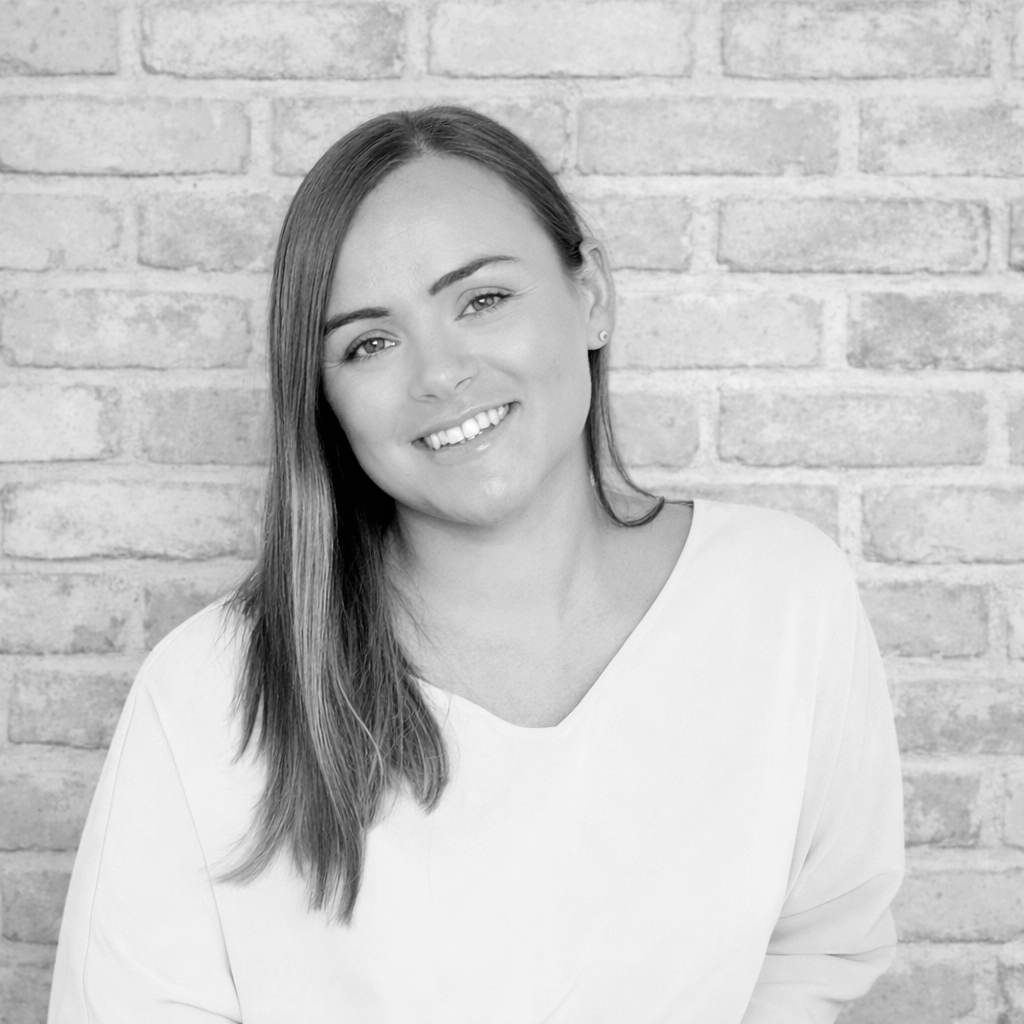 Portrait of a young woman with long hair, smiling, standing in front of a brick wall.