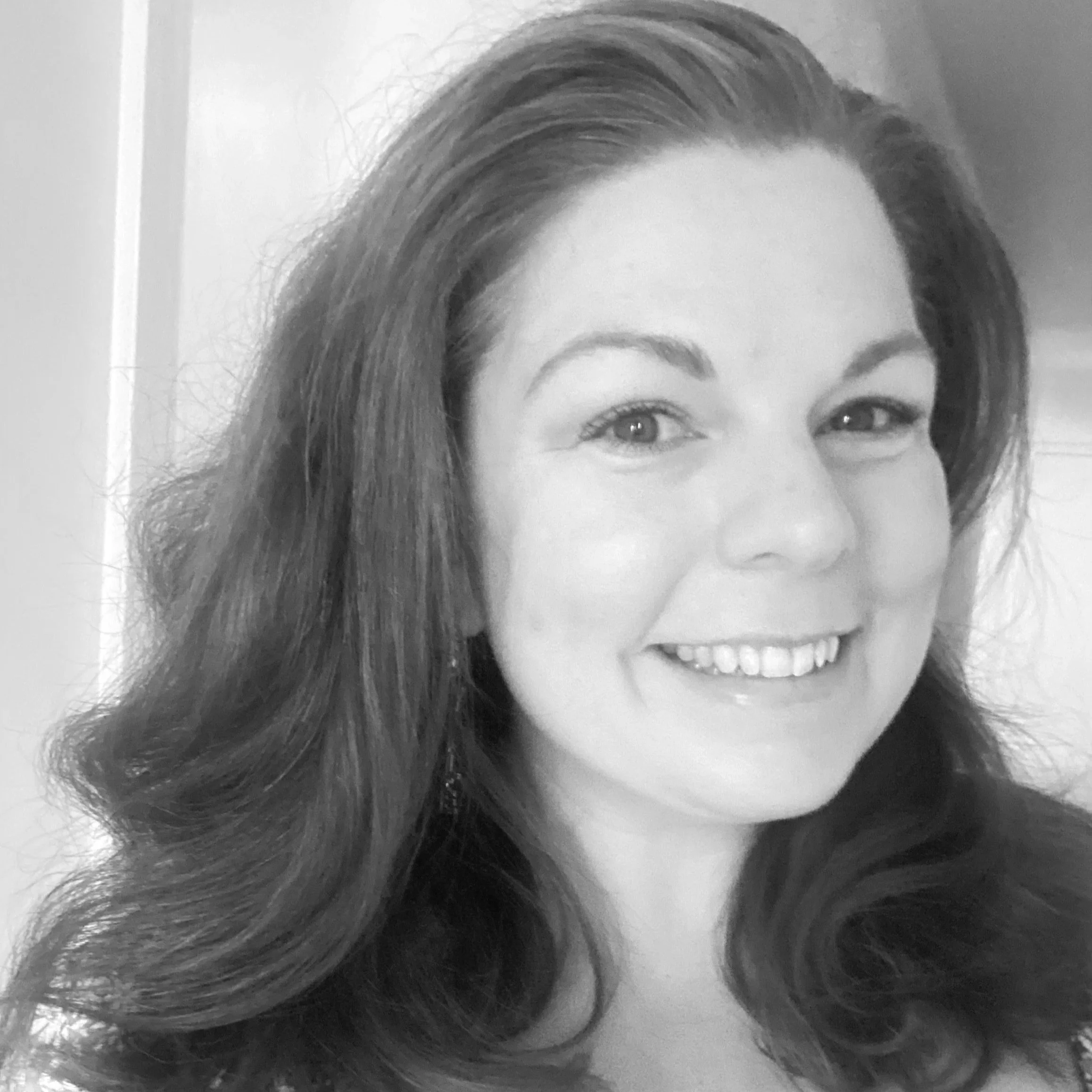 Black and white portrait of a woman with long wavy hair smiling at the camera.