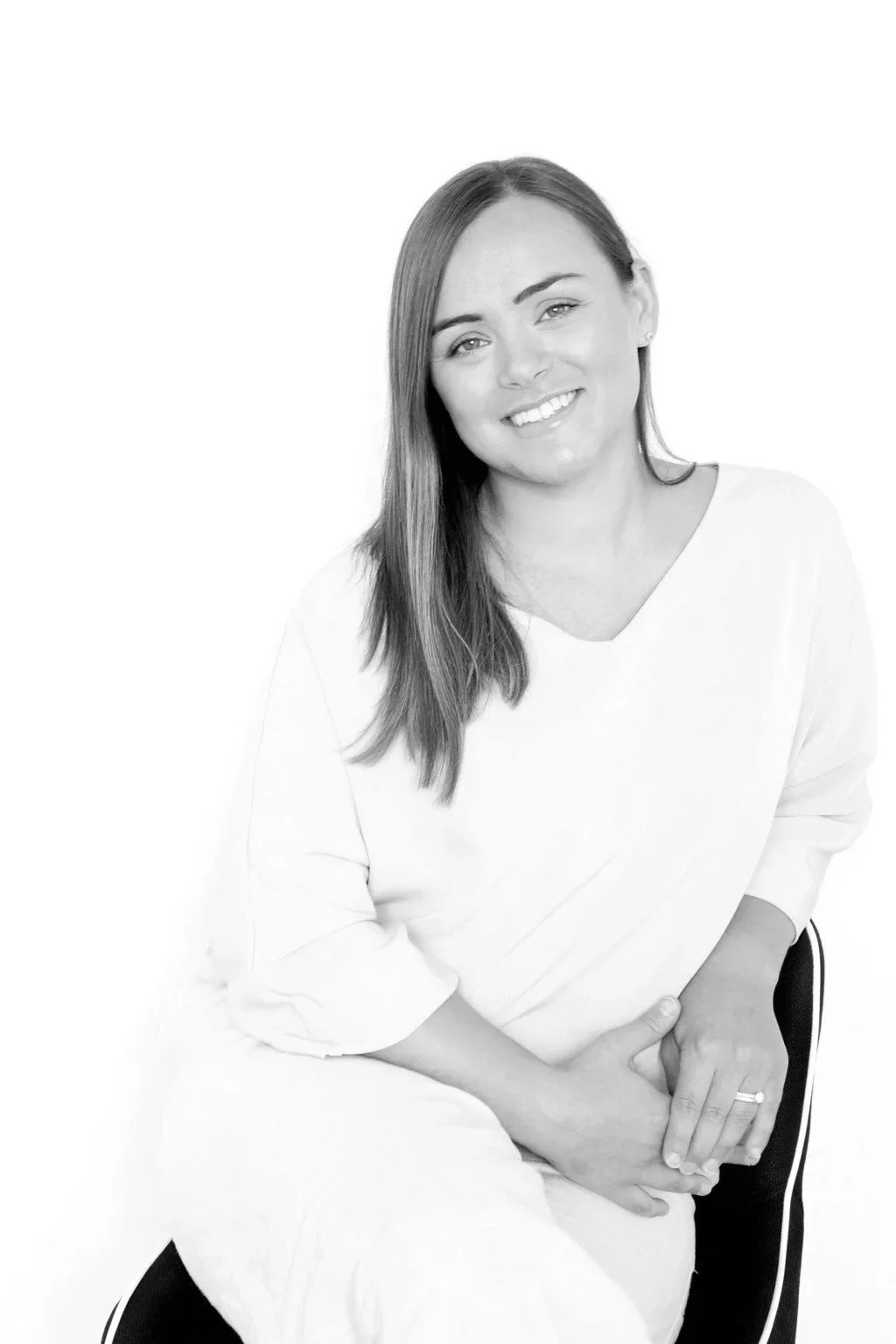 Black and white portrait of a woman with long hair smiling, sitting on a chair, wearing a long-sleeve top and striped pants.