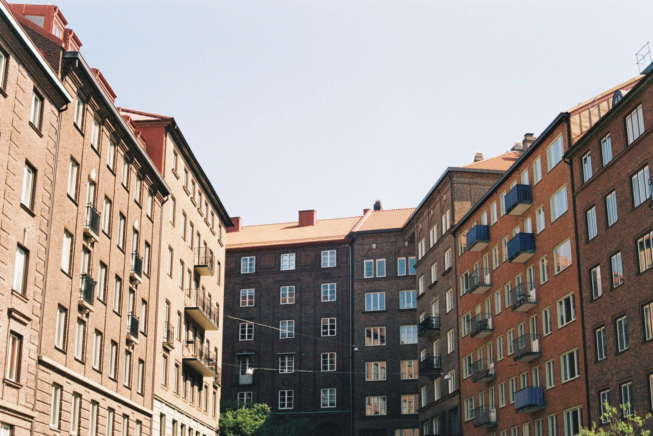 Flera höga, äldre tegelhus i stadsdel, med små balkonger och fönster, under en klar, blå himmel.