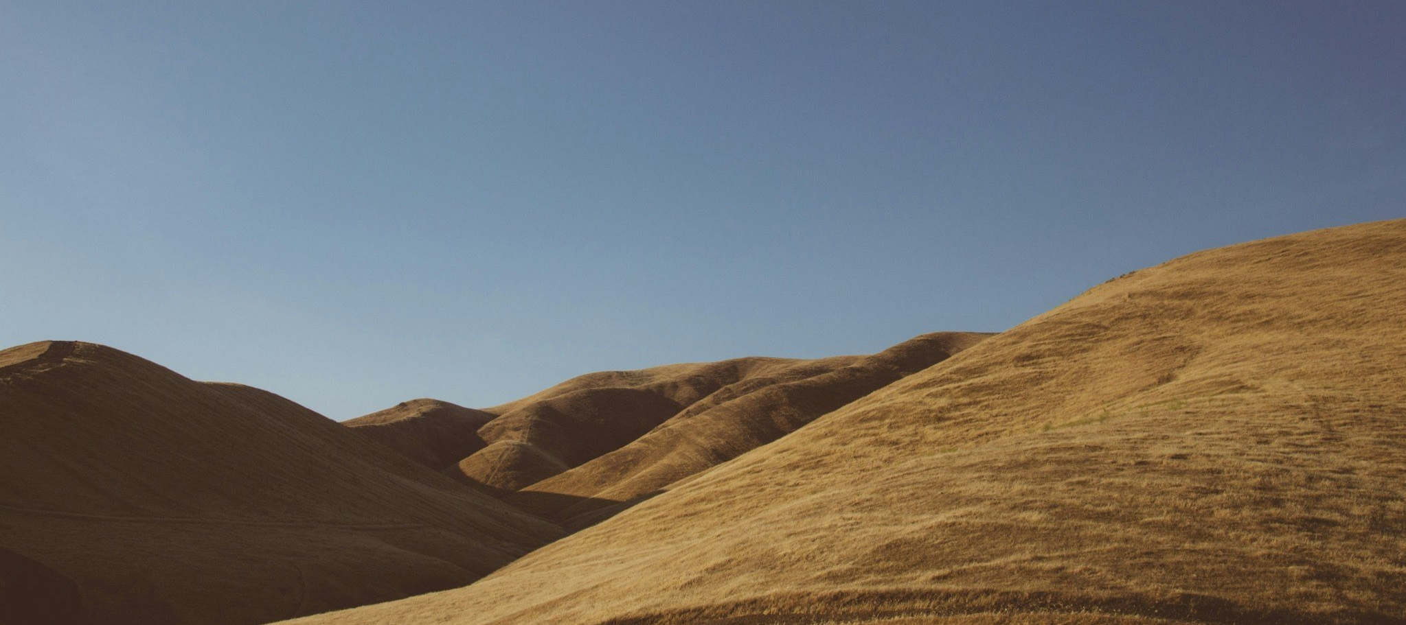 Hills covered with dry, yellow grass under a clear blue sky. Reminds us that our Speech Pathology and Occupational Therapy services provide access, empathy and hope to Ipswich and Springfield regions.
