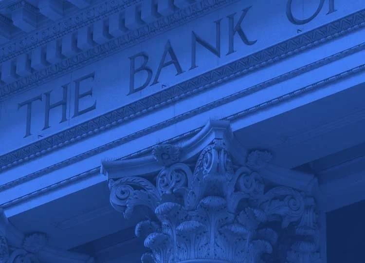 Close-up of the top of a Corinthian column in front of a sign that reads 'THE BANK OF'.