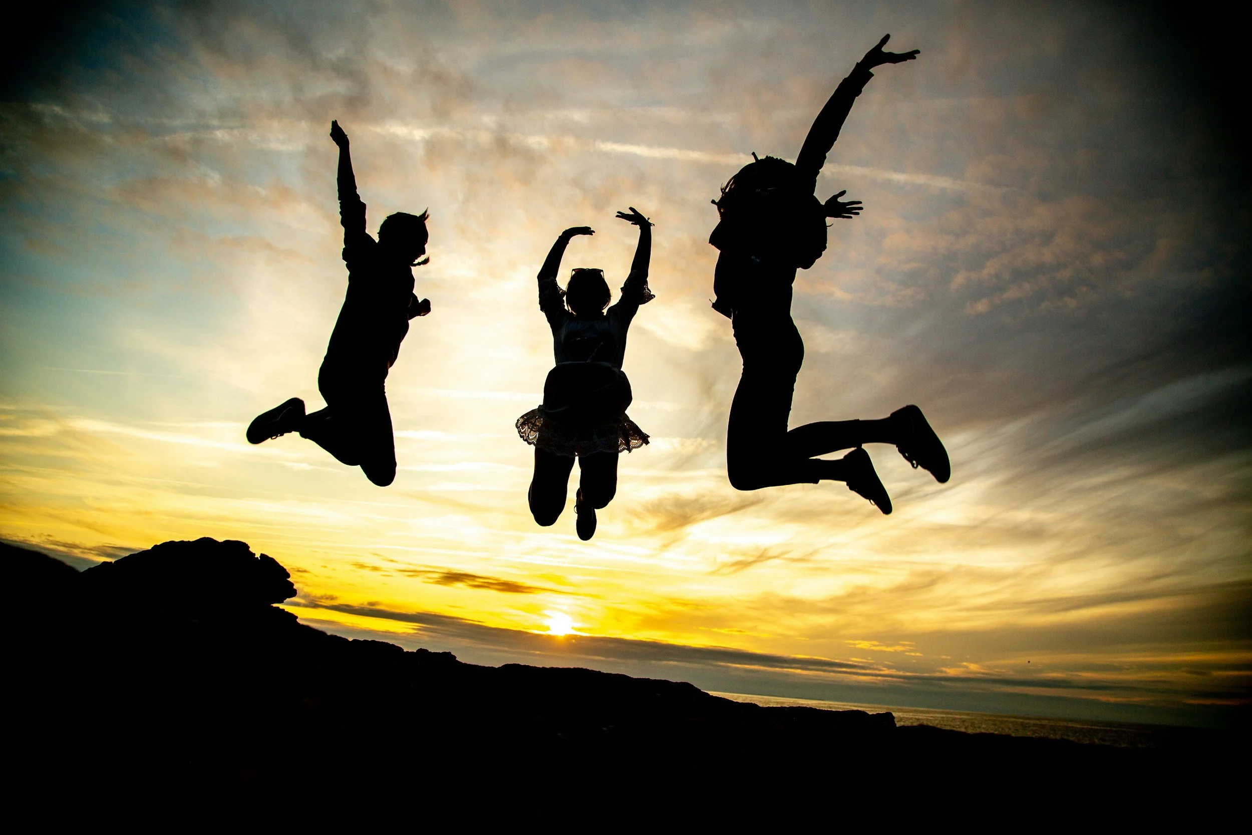 Silhouettes of four children jumping at sunset, with mountains in the background and a colorful sky.
