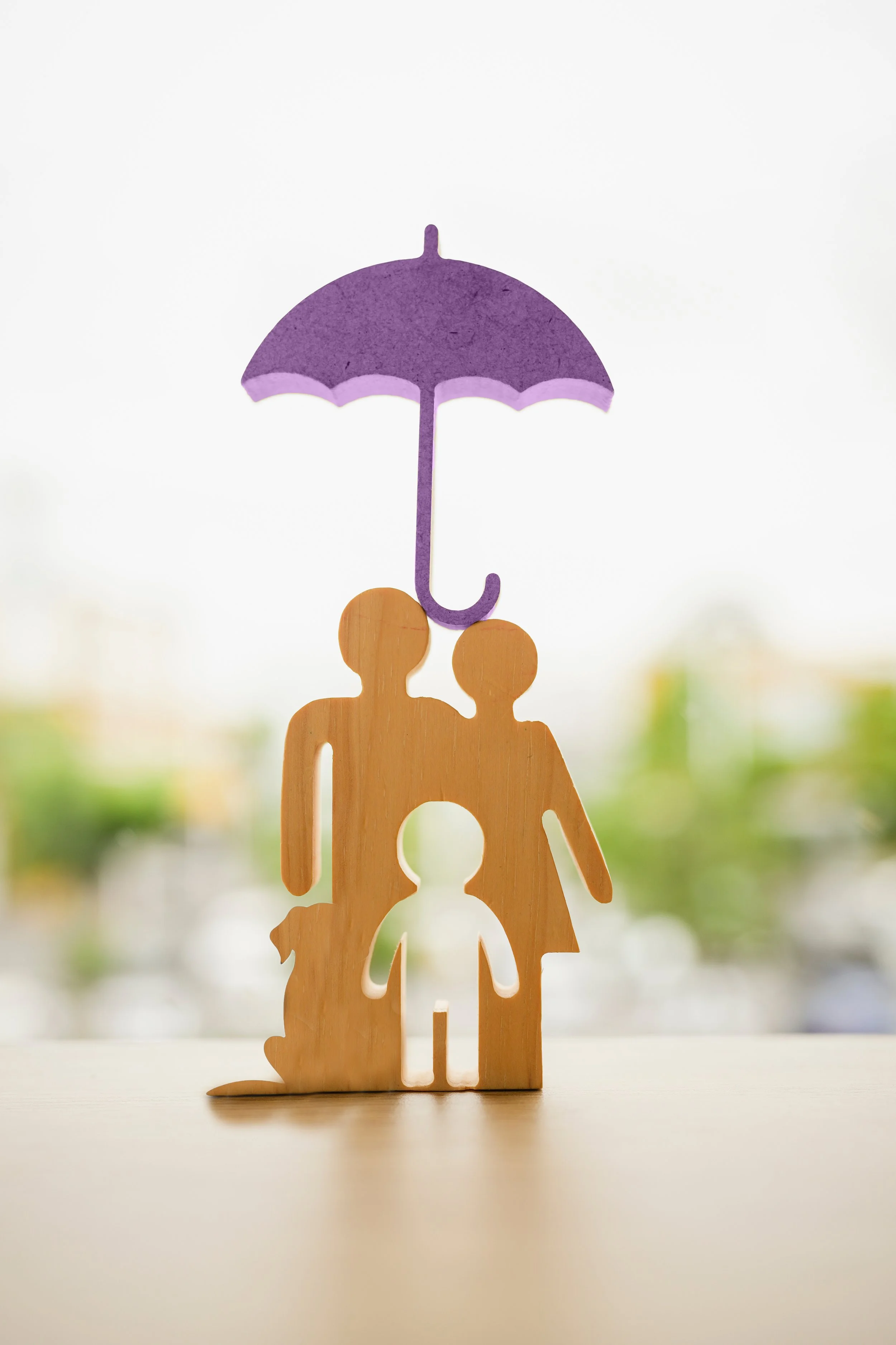 Wooden cutouts of a family and a dog with a purple umbrella held above them.