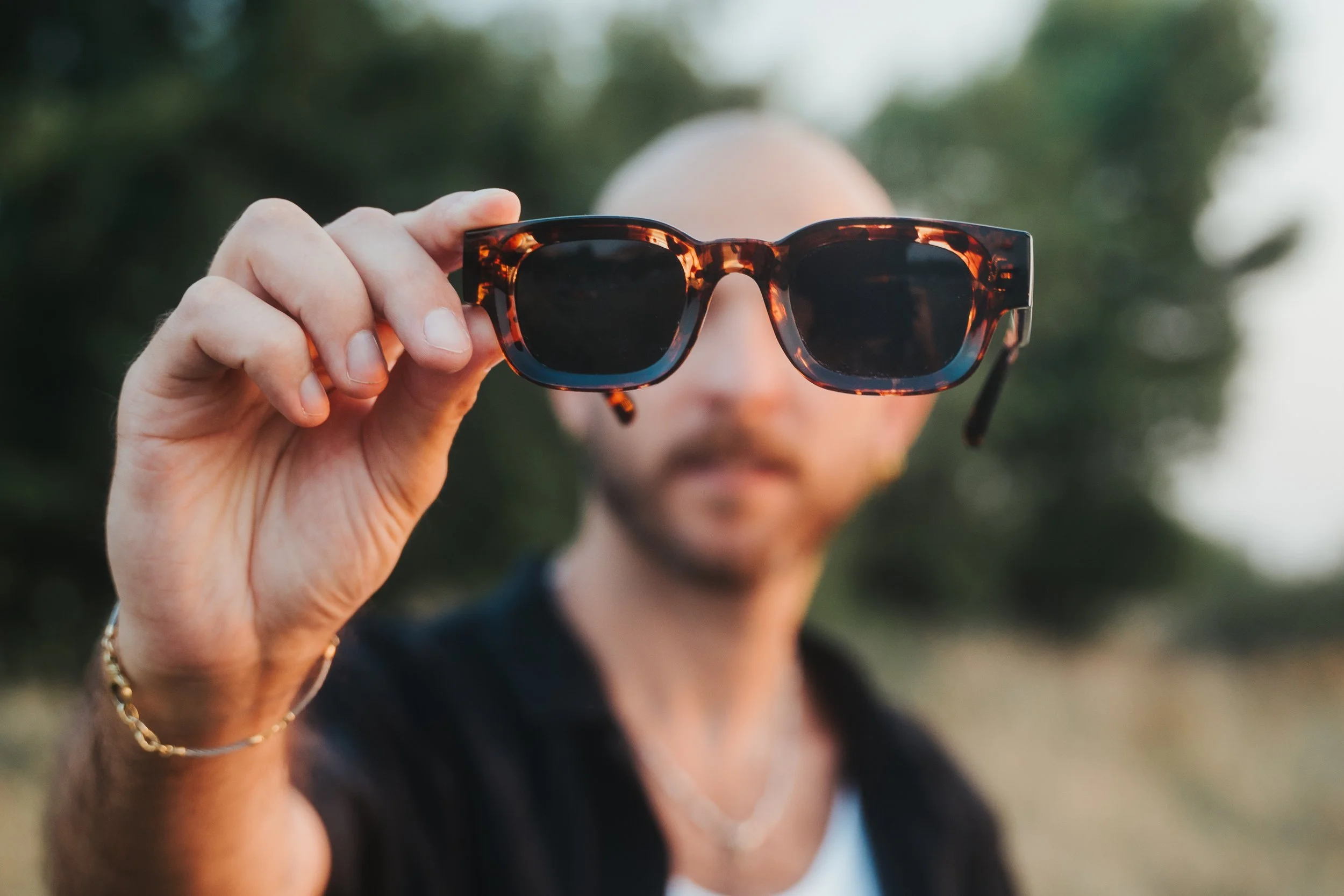 Man holding tortoiseshell sunglasses with blurred background.