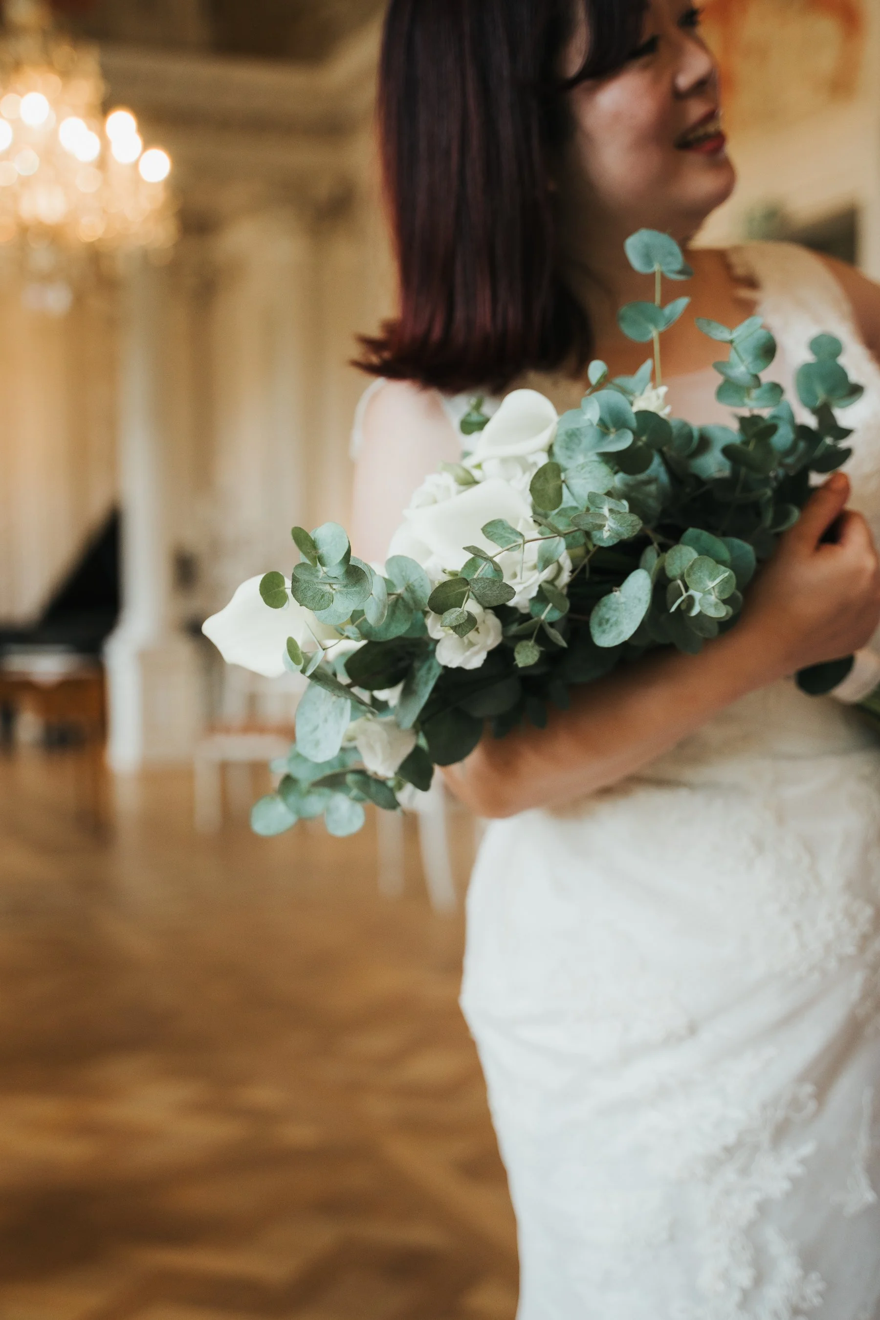 Bride holding eucalyptus and white calla lily bouquet in elegant indoor setting.