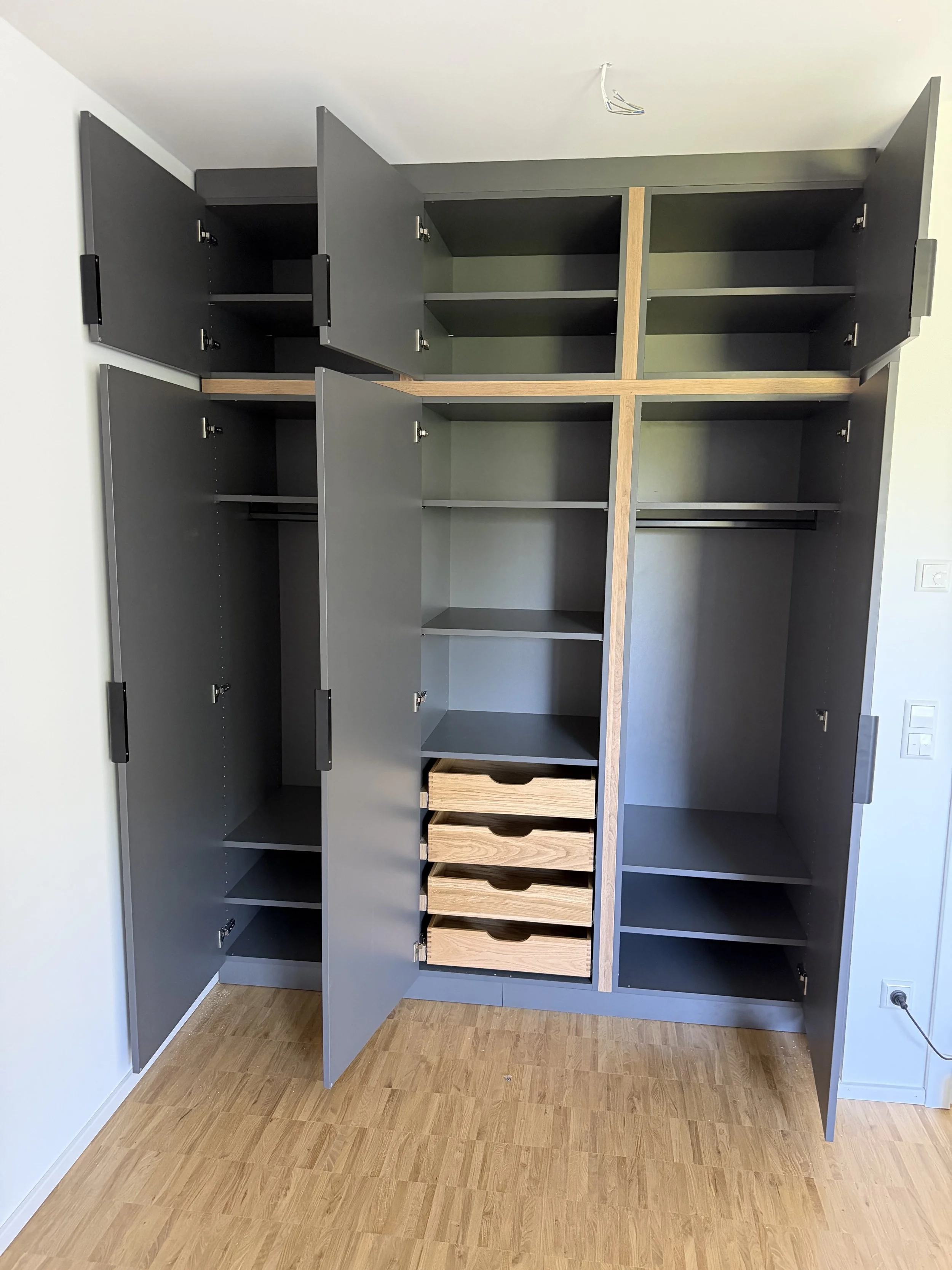 Ein schwarzer, offene Schrank mit mehreren Fächern, Schubladen und Schiebetüren, steht im Raum auf einem Holzboden.