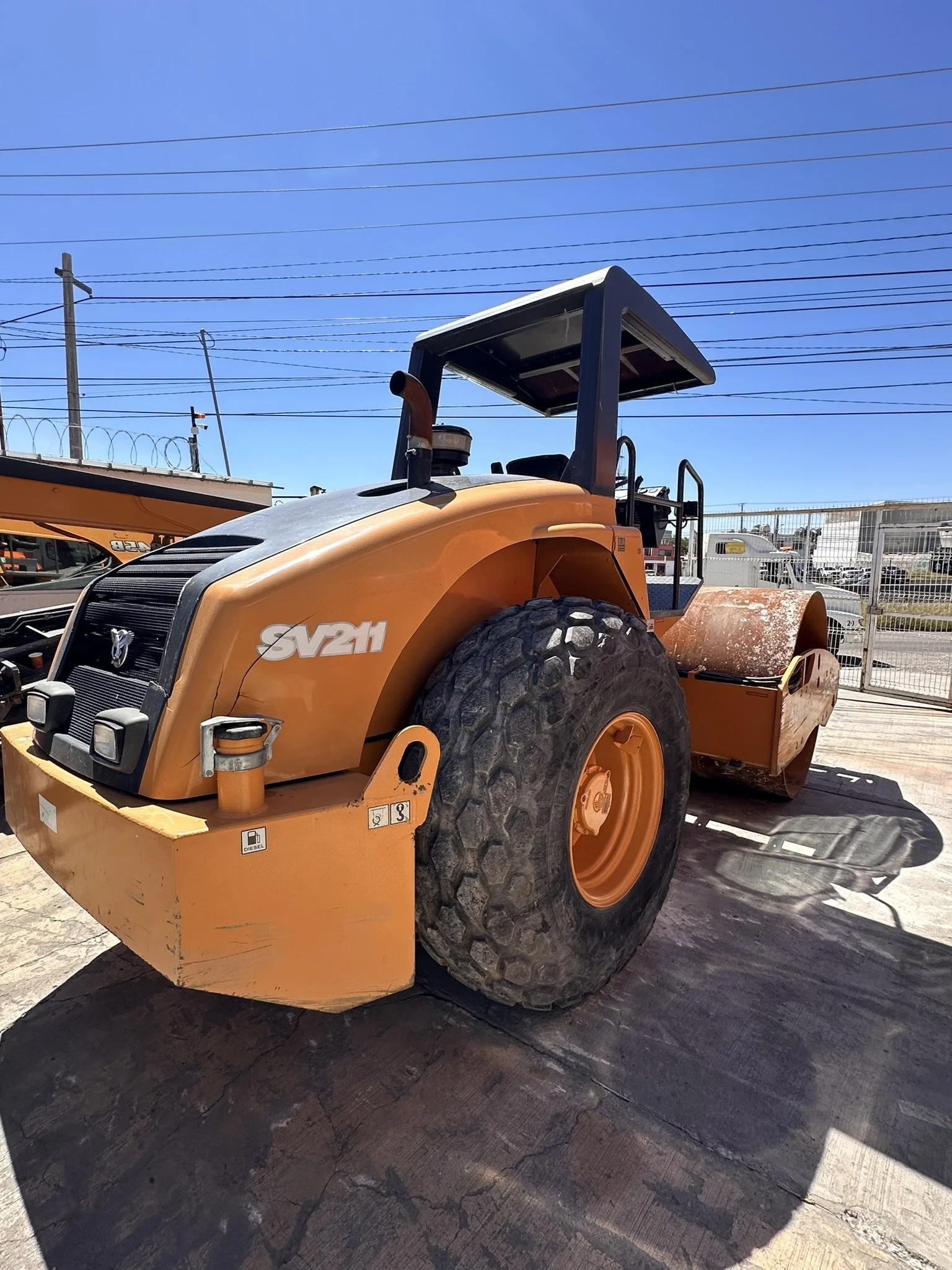 Rodillo compactador de color naranja estacionado en un área exterior y bajo un cielo despejado.