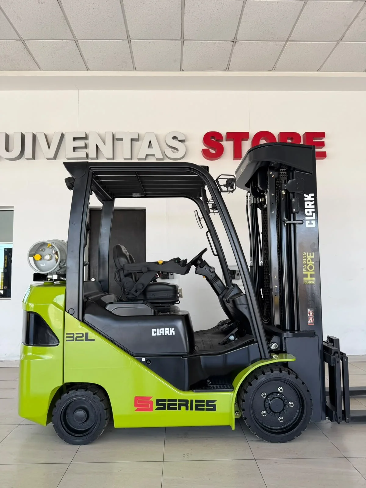 Montacargas verde y negro en un almacén, con rótulo que dice 'Suventas Store' en la pared de fondo.