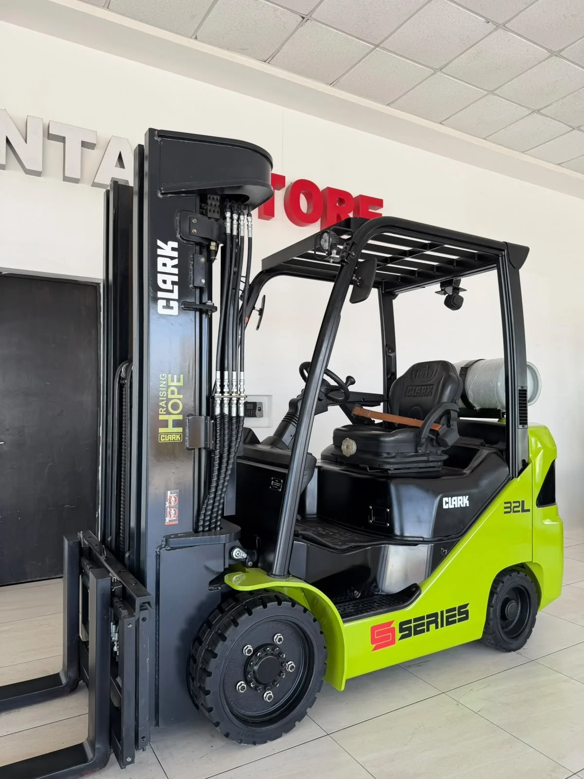 Montacargas eléctrico verde con asientos y mástil, en interiores de una tienda.