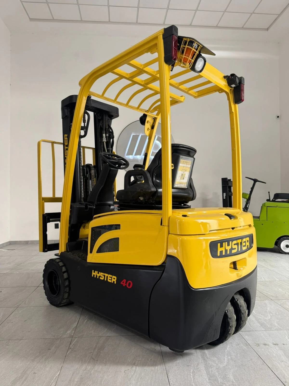 Montacargas amarillo con negro de la marca Hyster, modelo 40, ubicado en un espacio cerrado con piso de loseta. En el fondo, hay otra máquina de color verde.