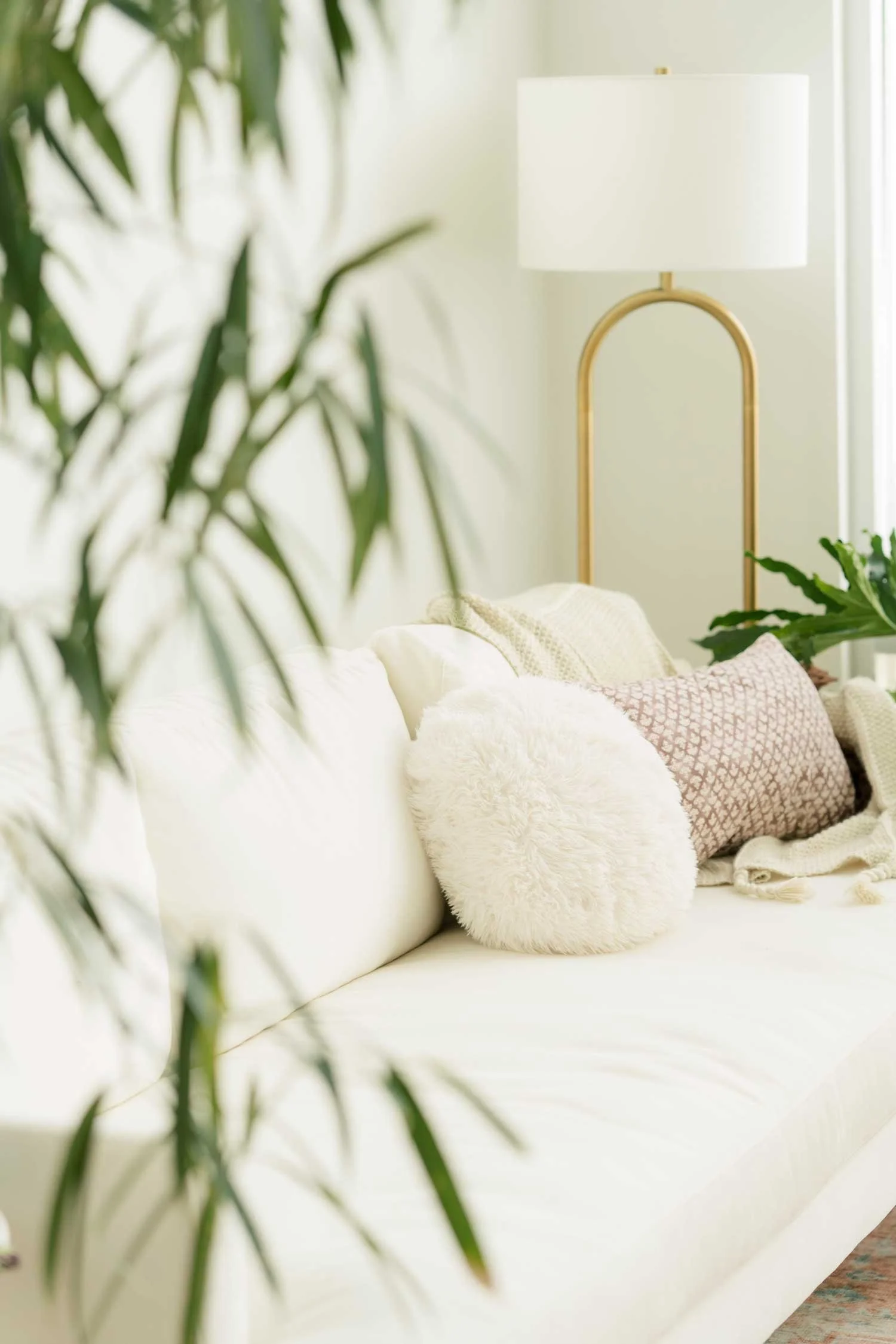Cozy therapy office with white sofa, fluffy pillows, plants, and a modern lamp.
