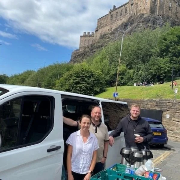 Three Charles White employees in front of the care van with food and hot drinks for vulnerable people with Edinburgh Castle behind them.