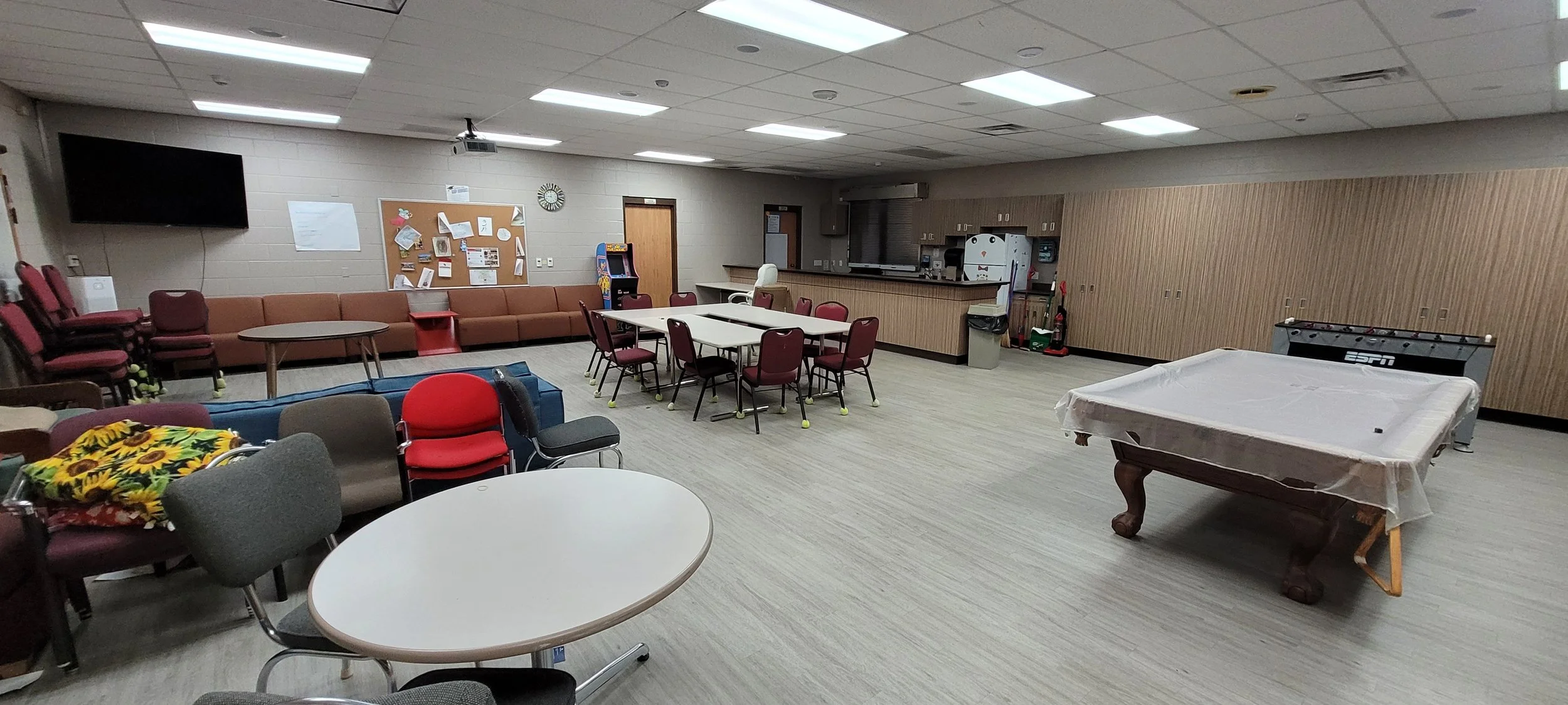 A room filled with different styles of chairs and tables, a pool table, a foosball table, counter space, and couches.