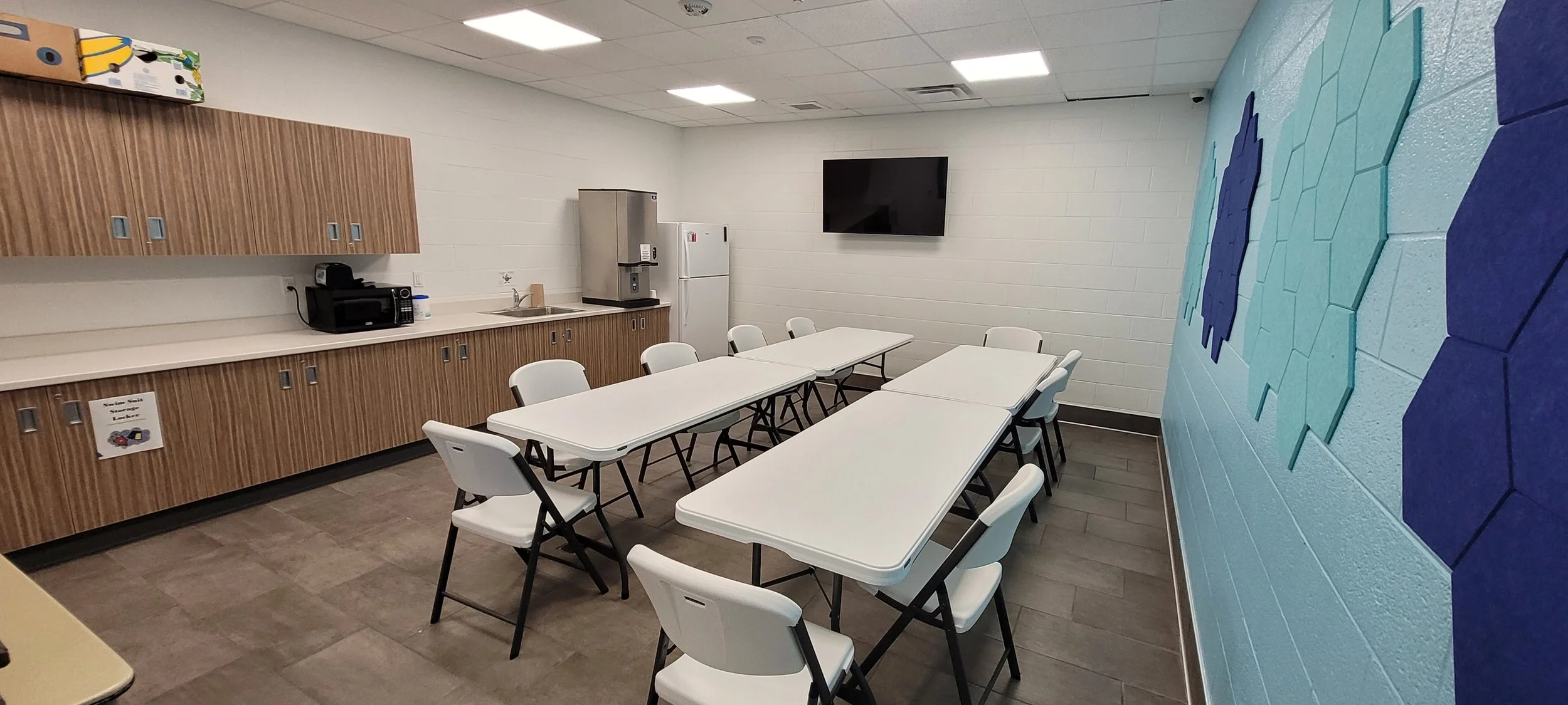 Meeting space with tiled floors, a tv mounted on the wall, tables and chairs, and a fridge and counters